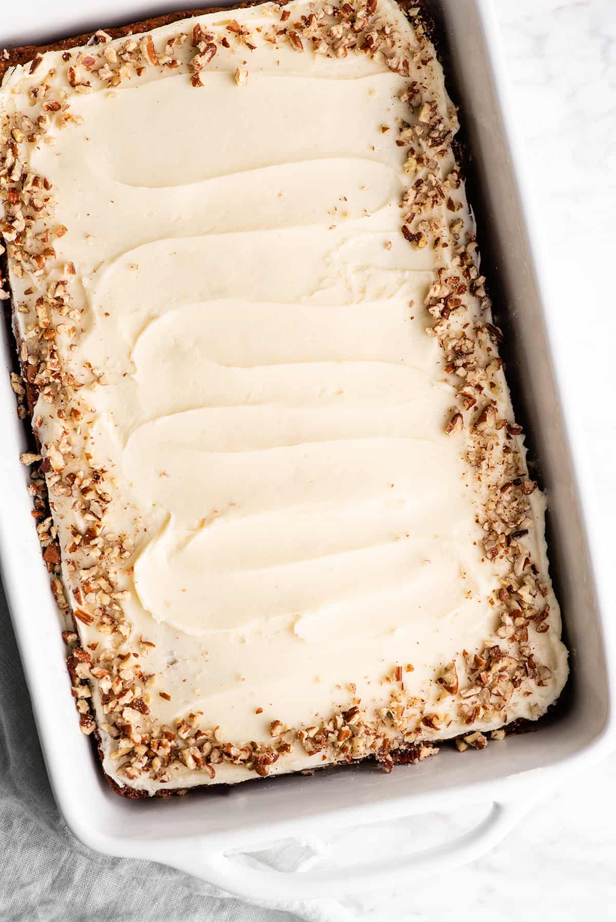 This is the best banana cake recipe ever! It's easy to make (no mixer required), moist, loaded with bananas and topped with a delicious cream cheese frosting. overhead view of a frosted banana cake in a pan with nuts around the edge