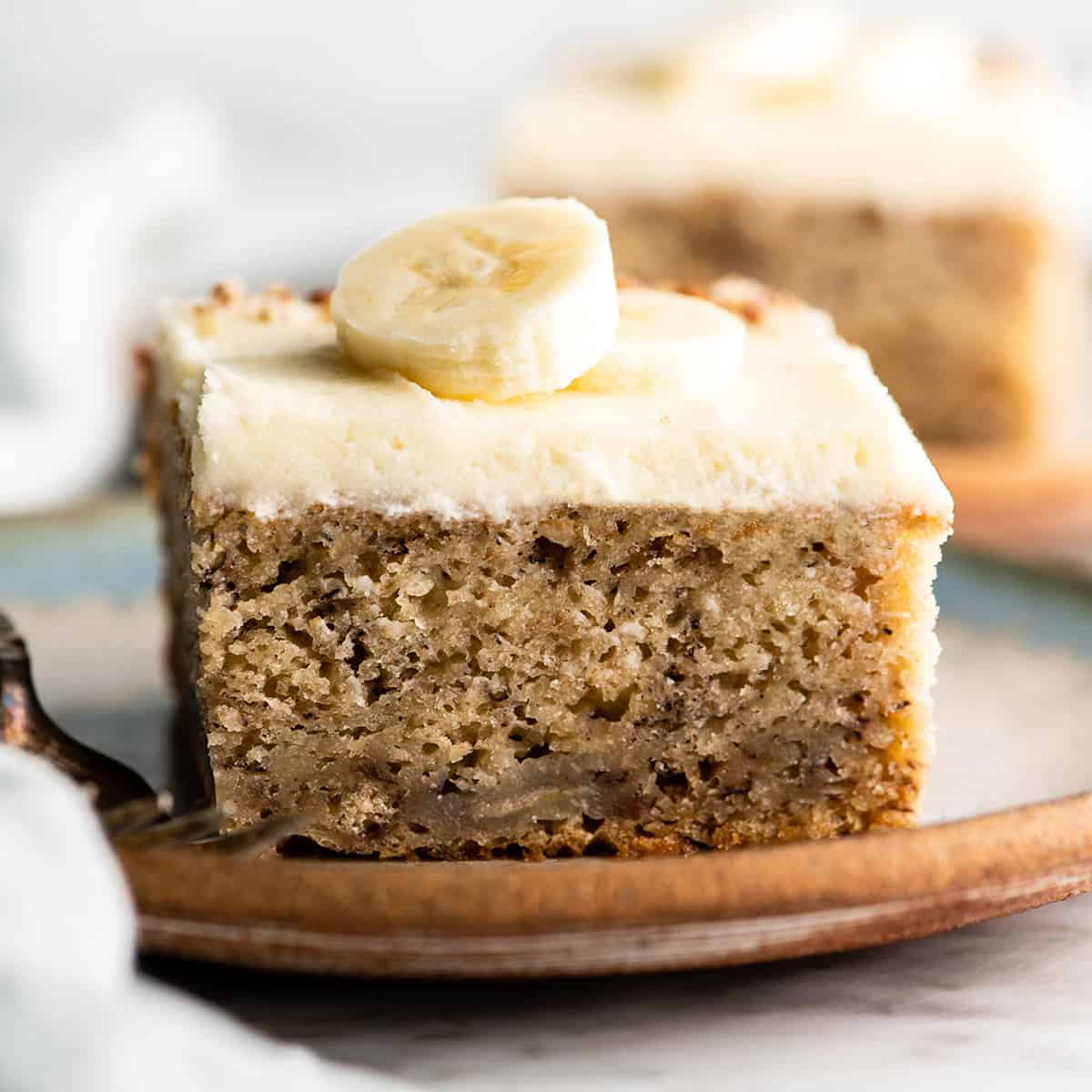 This is the best banana cake recipe ever! It's easy to make (no mixer required), moist, loaded with bananas and topped with a delicious cream cheese frosting. front view of a piece of banana cake with cream cheese frosting