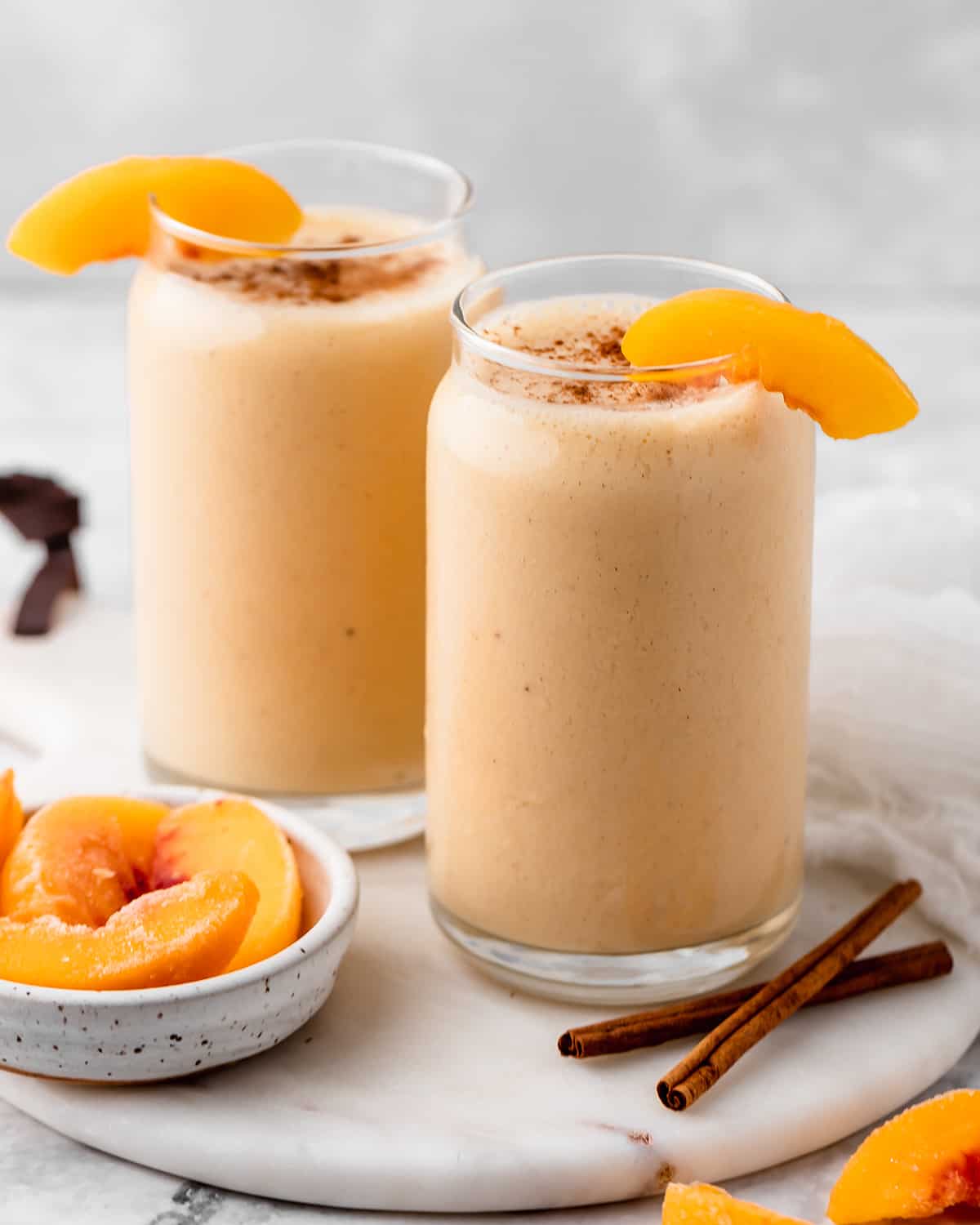two glasses of Peach Smoothie garnished with peach slices and sprinkled with cinnamon