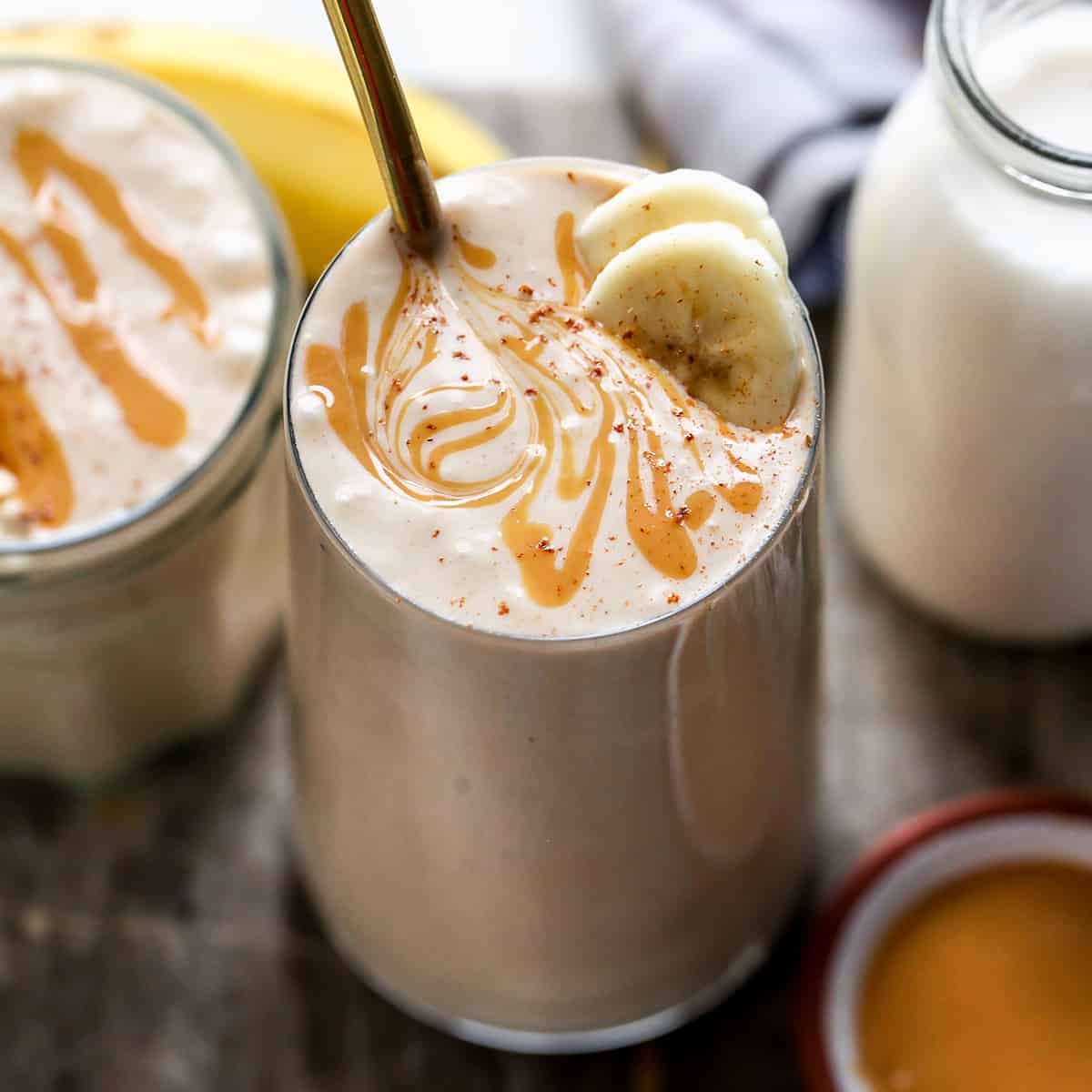 glass of Banana Peanut Butter Smoothie topped with cinnamon, peanut butter swirl and two slices of banana