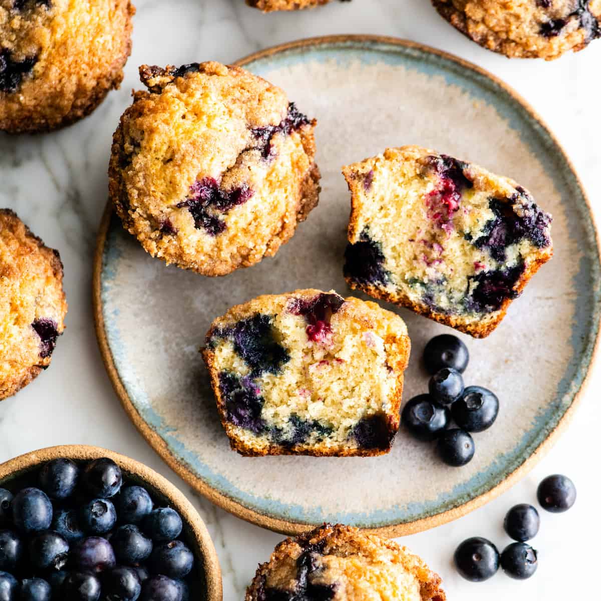 These are the best blueberry muffins ever! This blueberry muffin recipe results in moist, buttery blueberry muffins with a perfect texture that are loaded with fresh blueberries and topped with a crumb topping. They're easy to make in only 30 minutes and no mixer required! #blueberrymuffins #muffins #recipe #joyfoodsunshine #breakfast #brunch overhead view of a blueberry muffin cut in half with other whole muffins around it