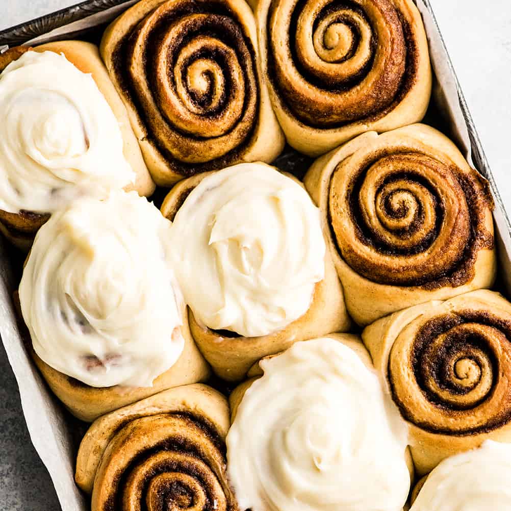 This is the Best Homemade Cinnamon Rolls Recipe EVER! These gooey cinnamon rolls are even better than Cinnabon cinnamon rolls, and are topped with a delicious cream cheese frosting! They're easy to make and can be prepared the day before and left to rise overnight in the refrigerator. overhead photo of 12 cinnamon rolls in a baking pan, some frosted some unfrosted