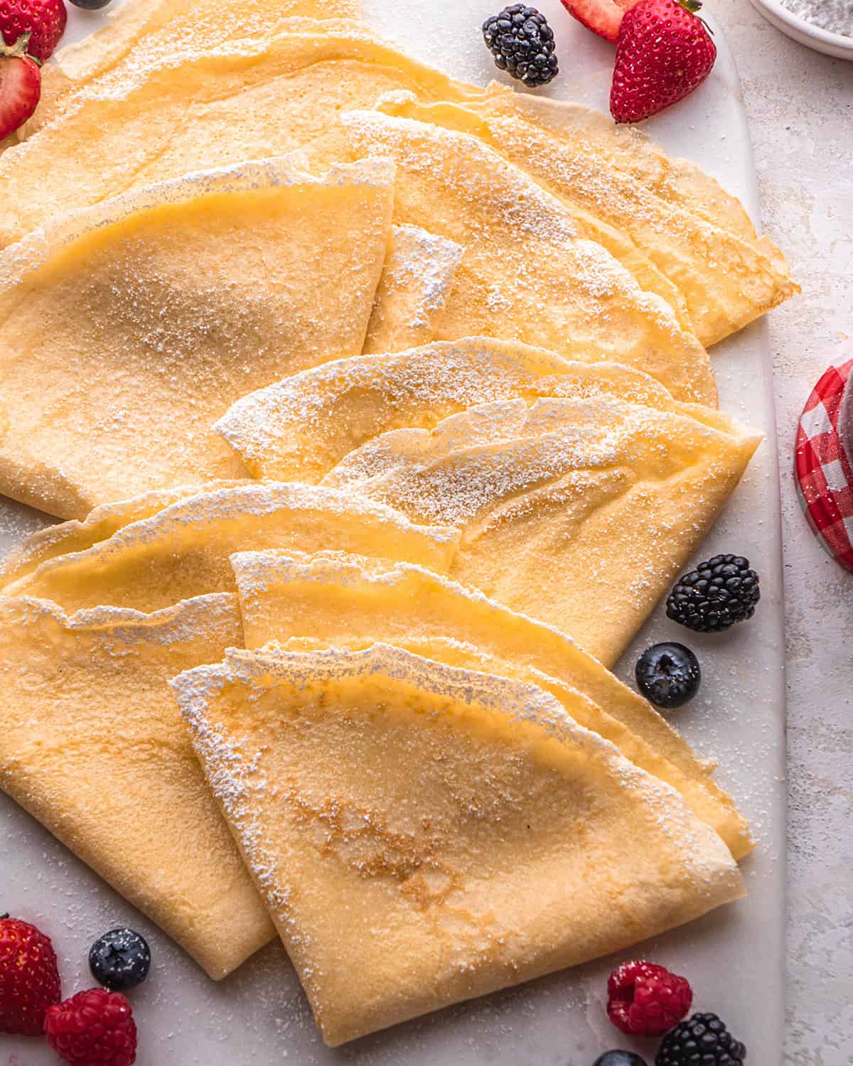 6 crepes folded into triangles on a serving platter dusted with powdered sugar