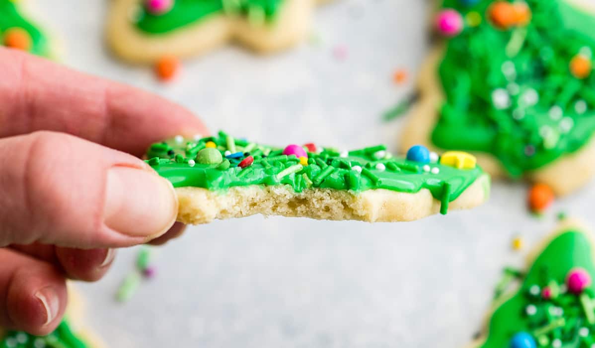 The Best Cut Out Sugar Cookie Recipe! They are soft, chewy and don't spread! Plus an easy sugar cookie frosting that tastes great and hardens with a beautiful shine that's perfect for decorating! Making these easy decorated sugar cookies has been our family's holiday baking tradition for 30 years! #sugarcookies #cutoutsugarcookies #christmascookies #christmas #baking #cutoutcookies #sugarcookiefrosting #recipe front view of a cut-outsugar cookie with a bite taken out of it