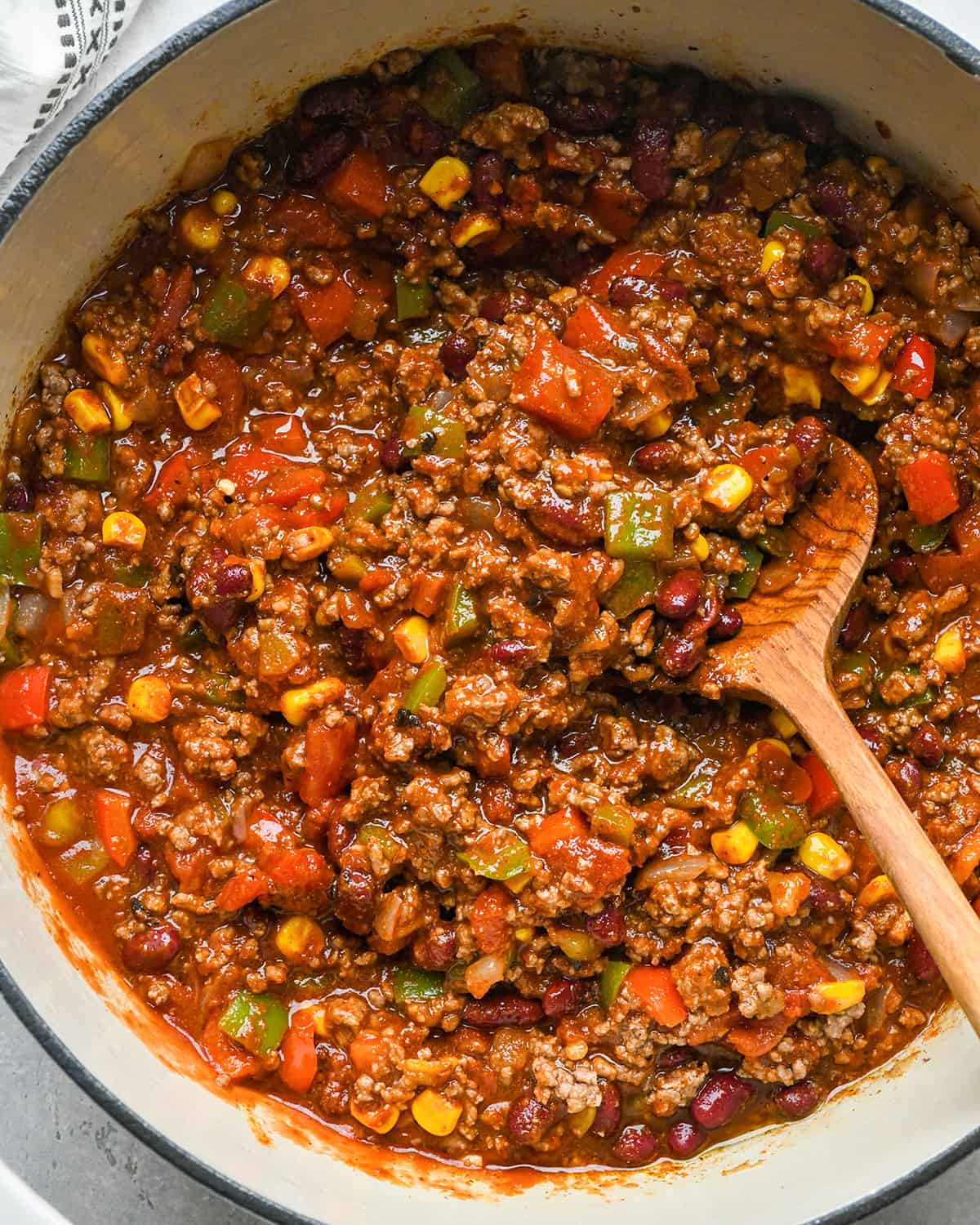 The BEST quick and easy chili recipe! Made in 30 minutes on the stovetop, this beef chili is the perfect easy, family-friendly dinner to enjoy while watching football in the fall! It's made from scratch (no packaged seasoning)! #chili #chilirecipe #fallfood #fallrecipe #beefchili #bestchili #easychili #quickchili best easy chili recipe in a pot with a wooden spoon