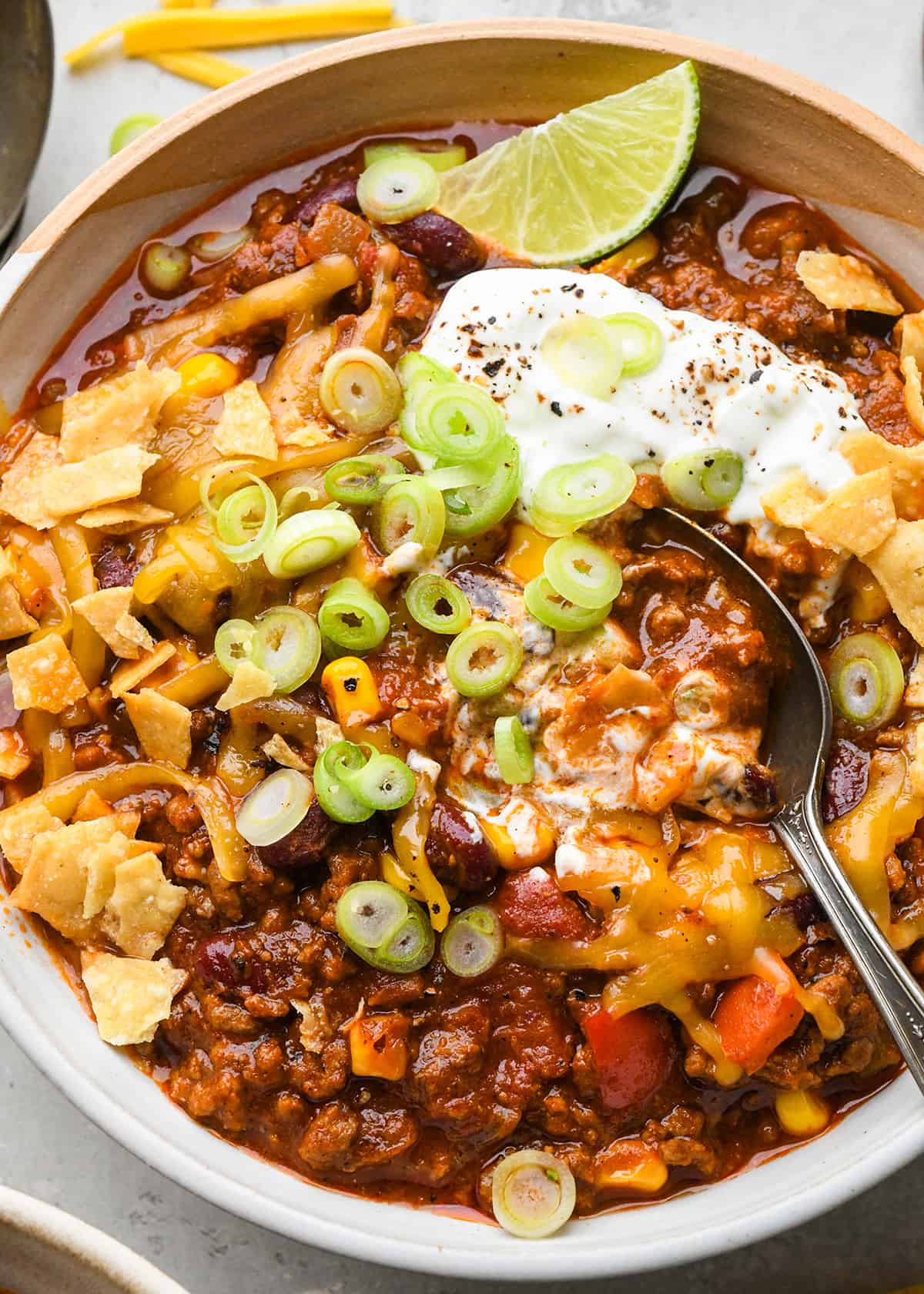 The BEST quick and easy chili recipe! Made in 30 minutes on the stovetop, this beef chili is the perfect easy, family-friendly dinner to enjoy while watching football in the fall! It's made from scratch (no packaged seasoning)! #chili #chilirecipe #fallfood #fallrecipe #beefchili #bestchili #easychili #quickchili homemade chili in a bowl with a spoon topped with sour cream, onions and cheese