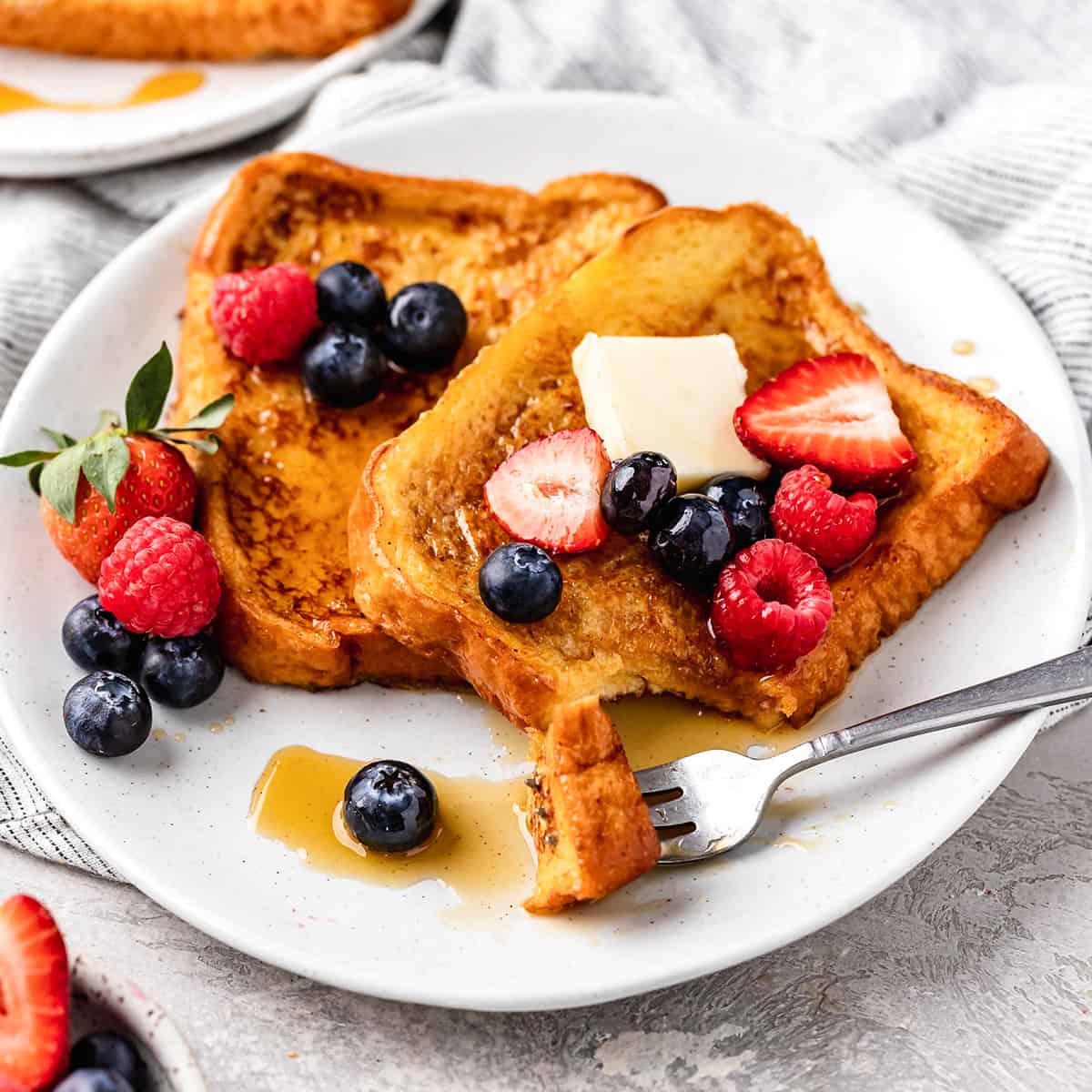 two pieces of French Toast on a plate with butter, syrup and berries