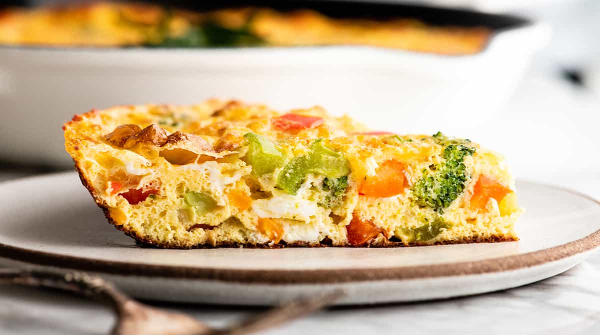 This easy Frittata Recipe is the perfect quick & healthy dinner, breakfast or brunch! Follow our step-by-step instructions and watch the video to learn how to make either a vegetable frittata or a frittata with bacon! side view of a slice of frittata on a plate