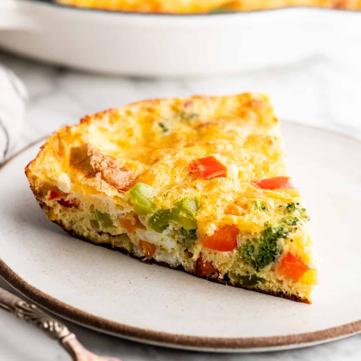 This easy Frittata Recipe is the perfect quick & healthy dinner, breakfast or brunch! Follow our step-by-step instructions and watch the video to learn how to make either a vegetable frittata or a frittata with bacon! front view of a piece of frittata on a plate