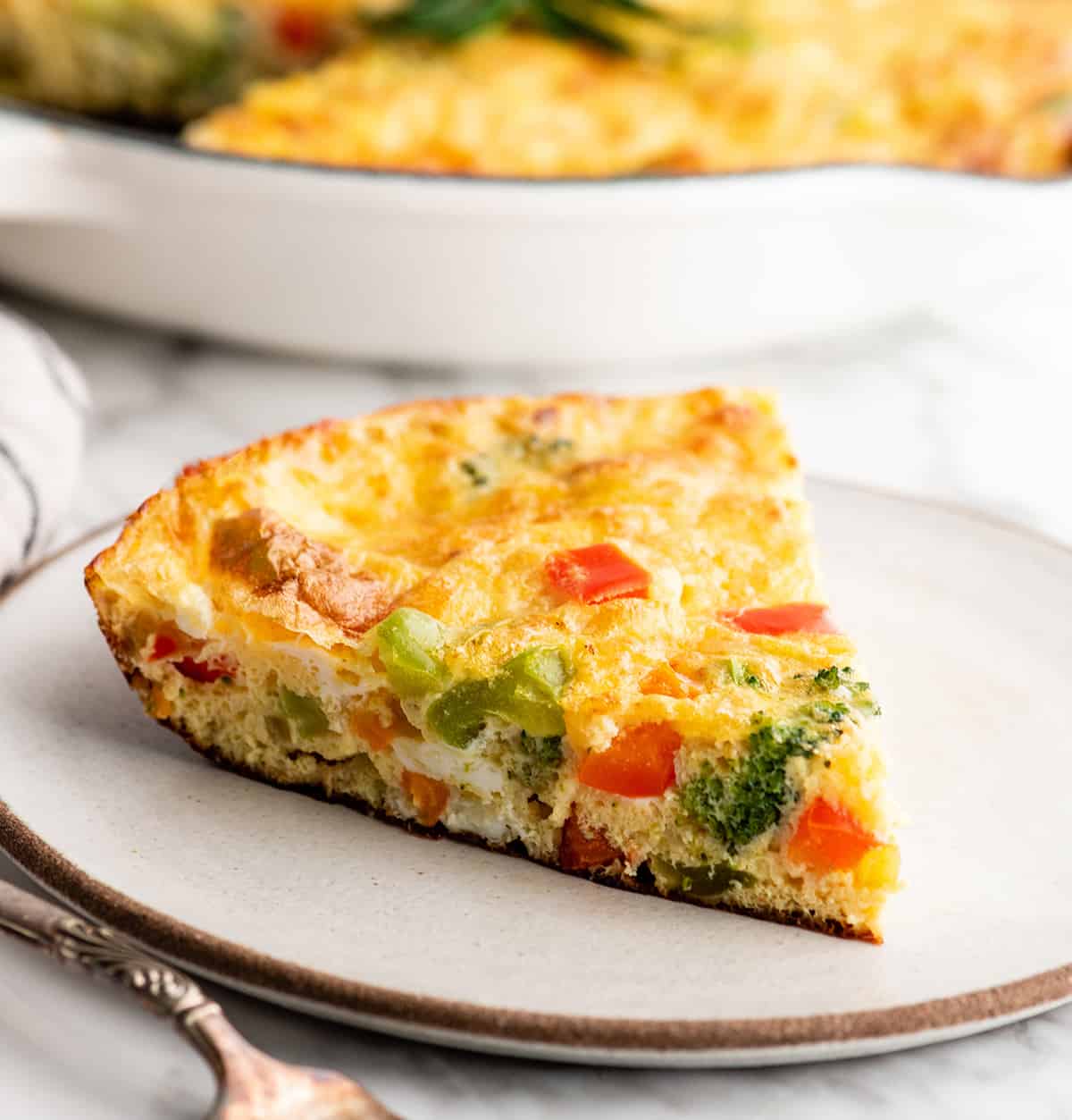 This easy Frittata Recipe is the perfect quick & healthy dinner, breakfast or brunch! Follow our step-by-step instructions and watch the video to learn how to make either a vegetable frittata or a frittata with bacon! front view of a slice of vegetable frittata on a plate
