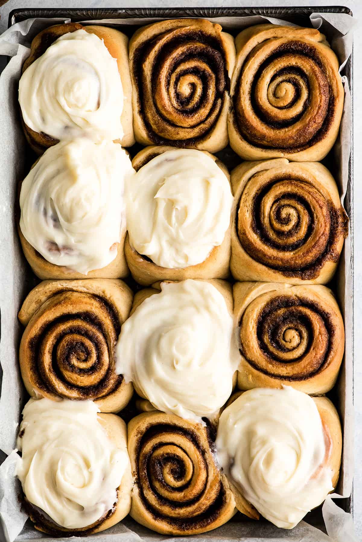 This is the Best Homemade Cinnamon Rolls Recipe EVER! These gooey cinnamon rolls are even better than Cinnabon cinnamon rolls, and are topped with a delicious cream cheese frosting! They're easy to make and can be prepared the day before and left to rise overnight in the refrigerator. overhead view of a pan of 12 homemade cinnamon rolls with cream cheese frosting