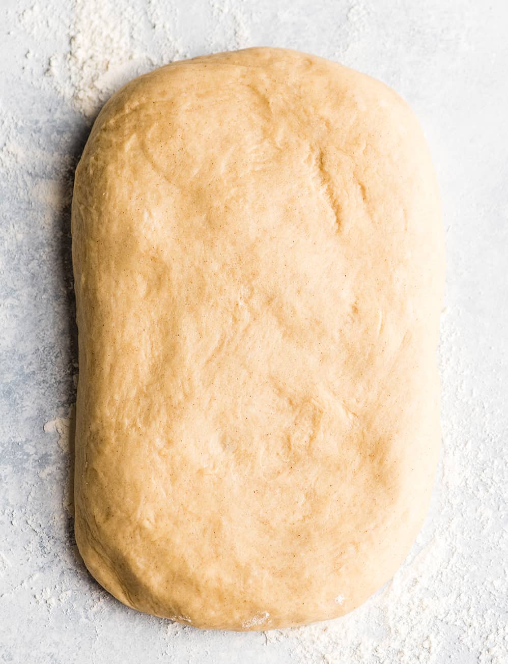 This is the Best Homemade Cinnamon Rolls Recipe EVER! These gooey cinnamon rolls are even better than Cinnabon cinnamon rolls, and are topped with a delicious cream cheese frosting! They're easy to make and can be prepared the day before and left to rise overnight in the refrigerator. overhead photo of cinnamon roll dough formed into a rectangle