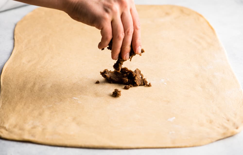 This is the Best Homemade Cinnamon Rolls Recipe EVER! These gooey cinnamon rolls are even better than Cinnabon cinnamon rolls, and are topped with a delicious cream cheese frosting! They're easy to make and can be prepared the day before and left to rise overnight in the refrigerator. cinnamon sugar filling being sprinkled onto cinnamon roll dough