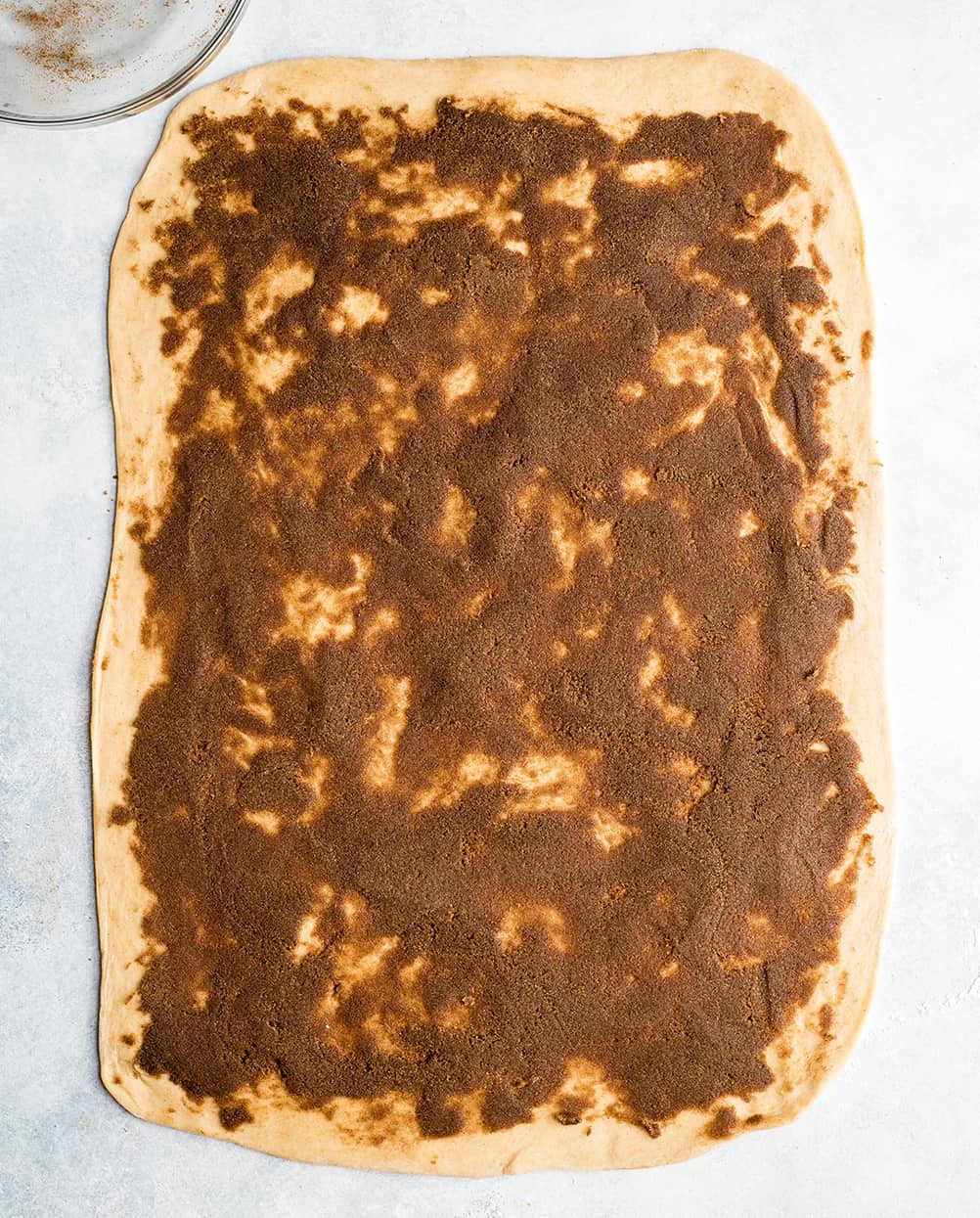 This is the Best Homemade Cinnamon Rolls Recipe EVER! These gooey cinnamon rolls are even better than Cinnabon cinnamon rolls, and are topped with a delicious cream cheese frosting! They're easy to make and can be prepared the day before and left to rise overnight in the refrigerator. overhead photo showing how to make cinnamon rolls - cinnamon sugar filling spread evenly over dough