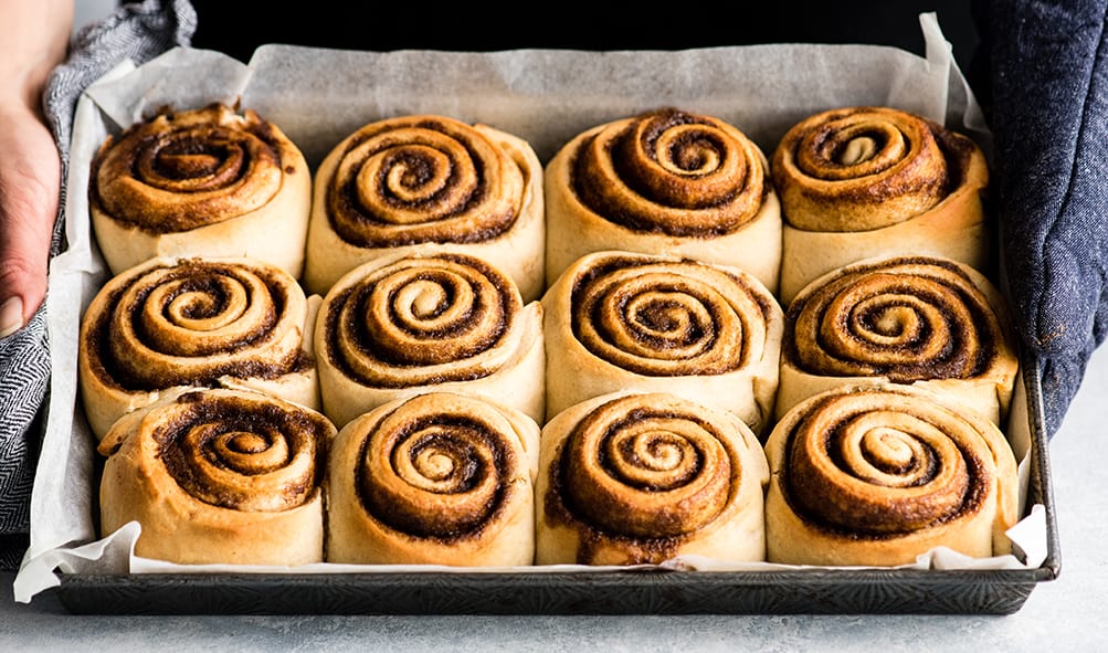 This is the Best Homemade Cinnamon Rolls Recipe EVER! These gooey cinnamon rolls are even better than Cinnabon cinnamon rolls, and are topped with a delicious cream cheese frosting! They're easy to make and can be prepared the day before and left to rise overnight in the refrigerator. front photo of hands holding a pan of baked cinnamon rolls