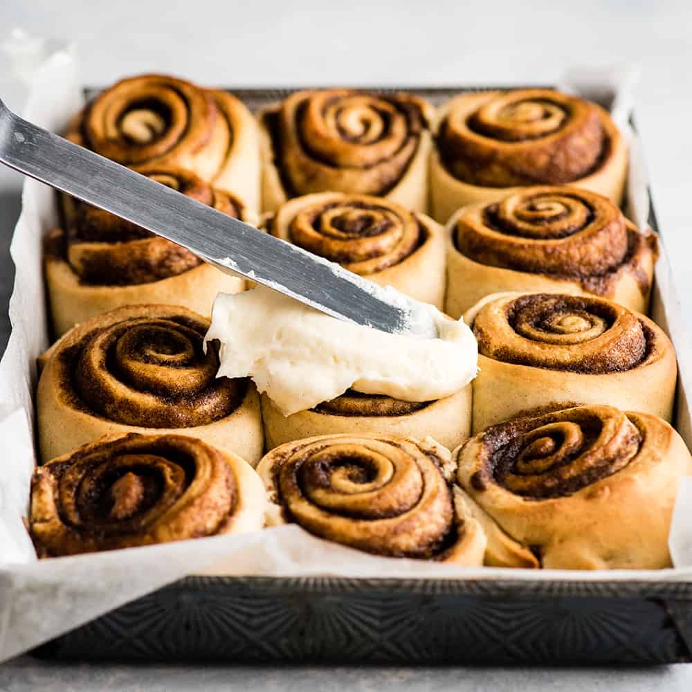 This is the Best Homemade Cinnamon Rolls Recipe EVER! These gooey cinnamon rolls are even better than Cinnabon cinnamon rolls, and are topped with a delicious cream cheese frosting! They're easy to make and can be prepared the day before and left to rise overnight in the refrigerator. front view of cinnamon rolls being frosted with cream cheese frosting