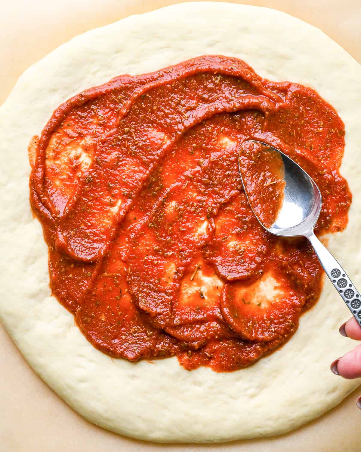 This is the best Easy Homemade Pizza Sauce Recipe ever! It's ready in 5 minutes and made with only 9 ingredients! Plus this healthy pizza sauce recipe is gluten-free, paleo-friendly, dairy-free, & vegan! #homemadepizza #pizzasauce #recipe #pizza #paleo pizza sauce being spread onto pizza dough with a spoon