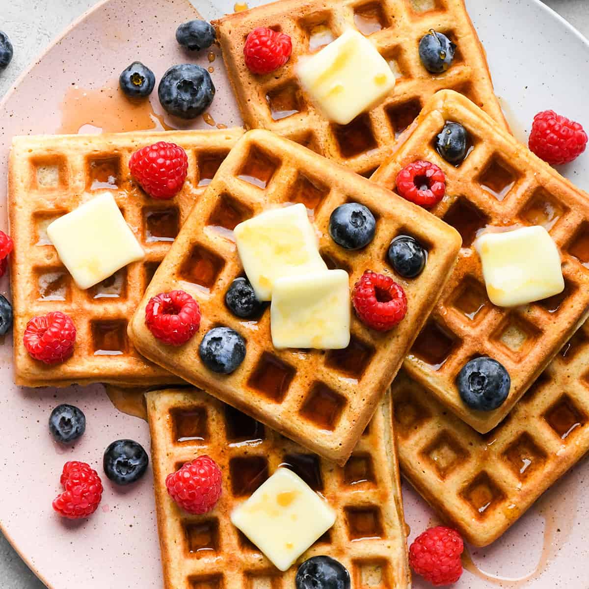 The Best Waffle Recipe EVER! These golden-brown, crispy, fluffy homemade waffles turn out perfectly every time! They're made completely from scratch, are freezer-friendly, and are lightened up by using applesauce in the batter! Plus this recipe makes a HUGE batch, so you will definitely have leftovers to enjoy all week long! 6 waffles on a plate with syrup, butter and berries