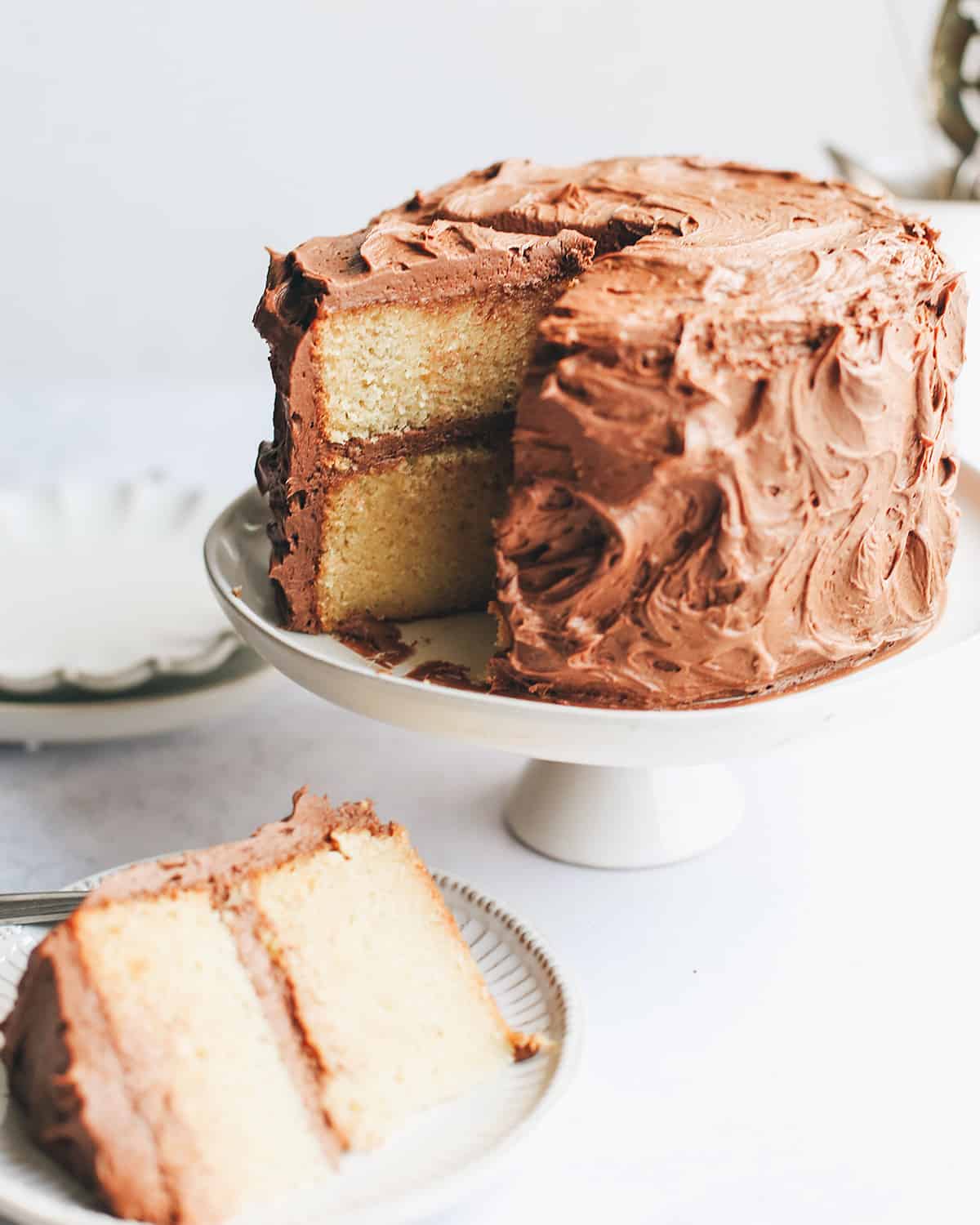 yellow cake on a cake plate with 2 slices cut out, one on a plate nearby