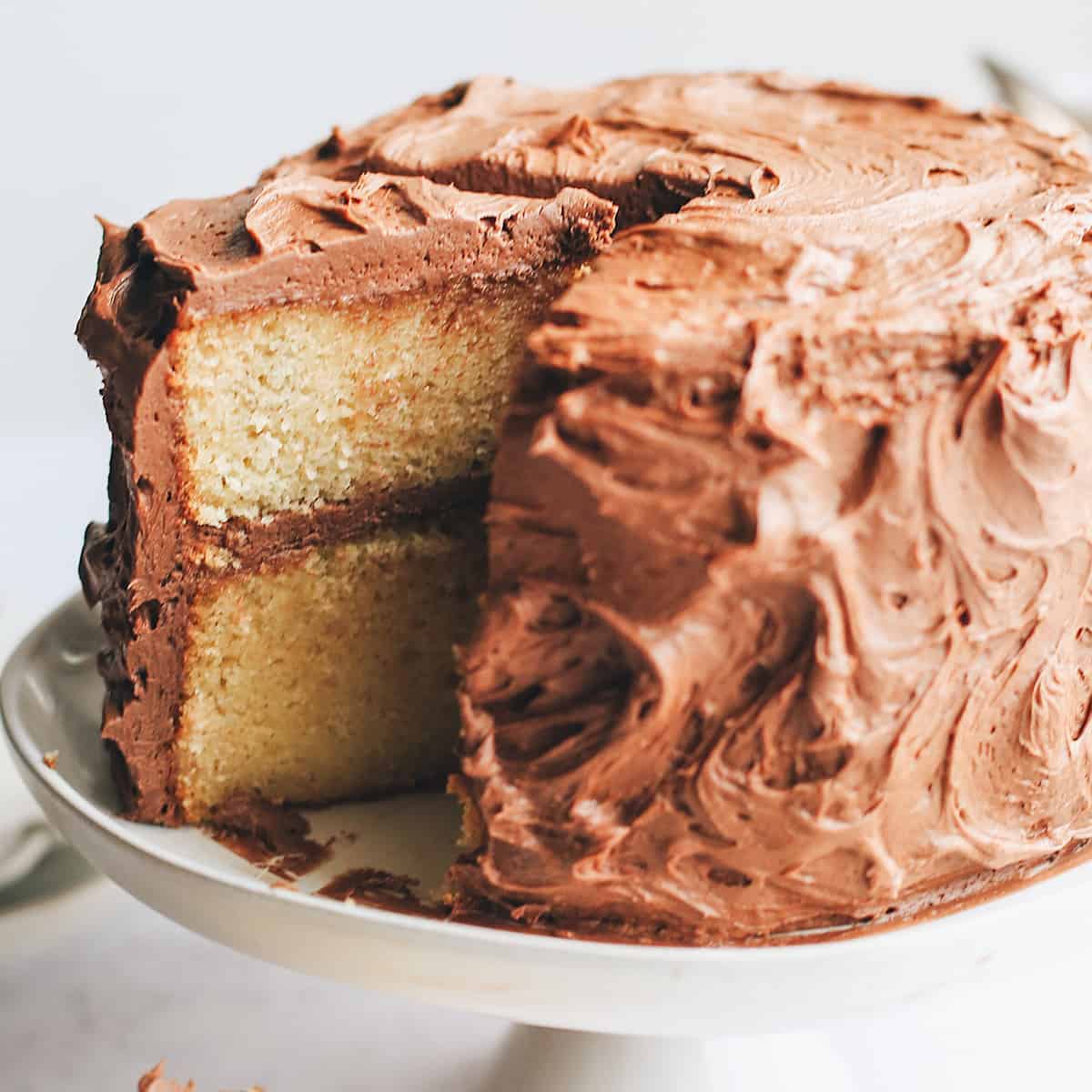 up close photo of a yellow cake on a cake plate with a slice cut out of it