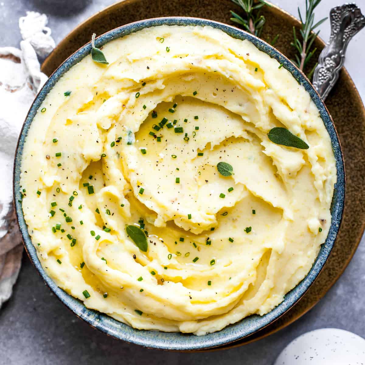 These herb-infused garlic mashed potatoes are the best mashed potatoes you will ever eat. They are creamy, fluffy buttery and so insanely delicious you will never make another mashed potatoes recipe again. Plus they're easy to make and can be prepared ahead of time! Overhead view of mashed potatoes in a bowl topped with fresh herbs