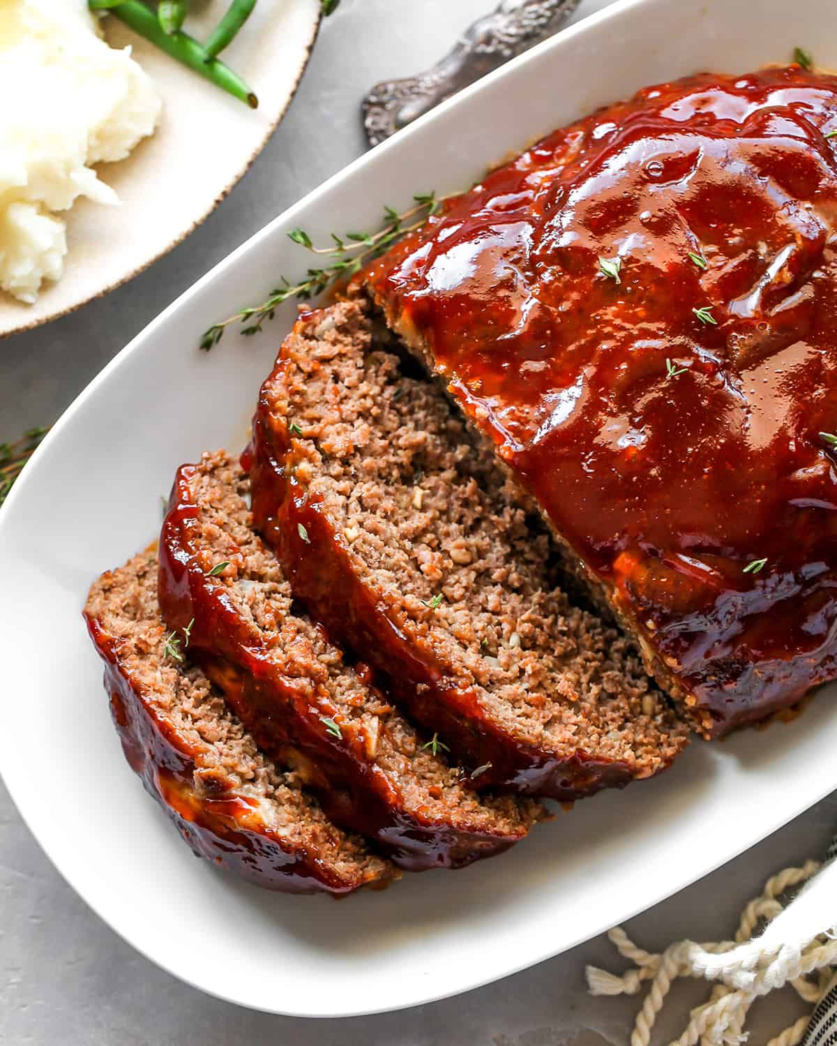 This is the best meatloaf recipe ever! It’s tender, moist and flavorful with the most delicious glaze. This easy meatloaf recipe is a classic that your whole family will love! Watch the video and follow our step-by-step instructions to learn how to make meatloaf! overhead view of the best meatloaf cut into slices on a serving platter