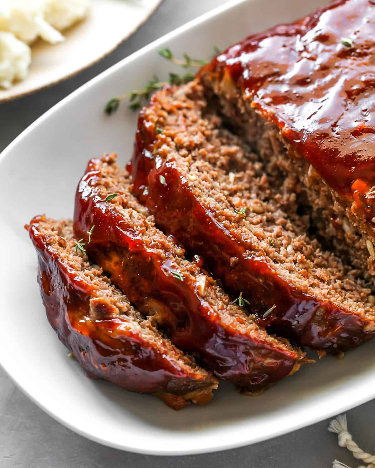 This is the best meatloaf recipe ever! It’s tender, moist and flavorful with the most delicious glaze. This easy meatloaf recipe is a classic that your whole family will love! Watch the video and follow our step-by-step instructions to learn how to make meatloaf! front view of slices of the Best Meatloaf Recipe on a platter