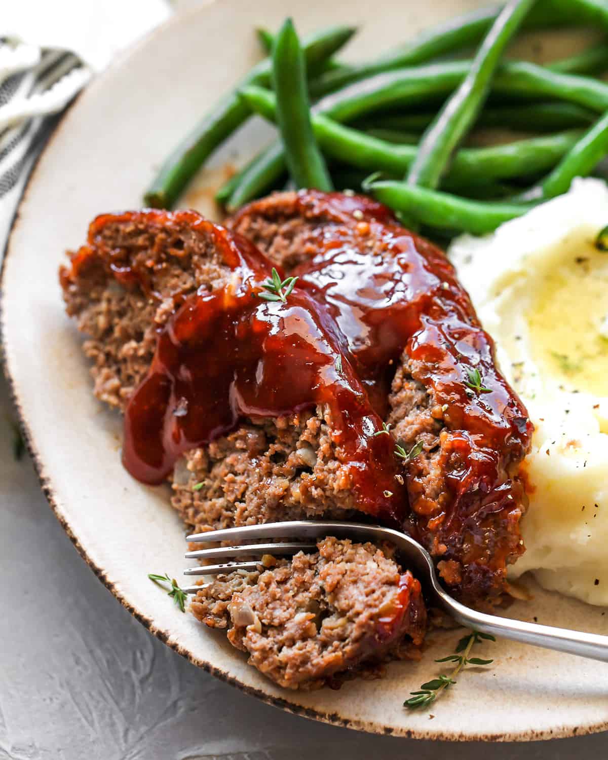 This is the best meatloaf recipe ever! It’s tender, moist and flavorful with the most delicious glaze. This easy meatloaf recipe is a classic that your whole family will love! Watch the video and follow our step-by-step instructions to learn how to make meatloaf! two slices of meatloaf on a plate with a fork taking a bite