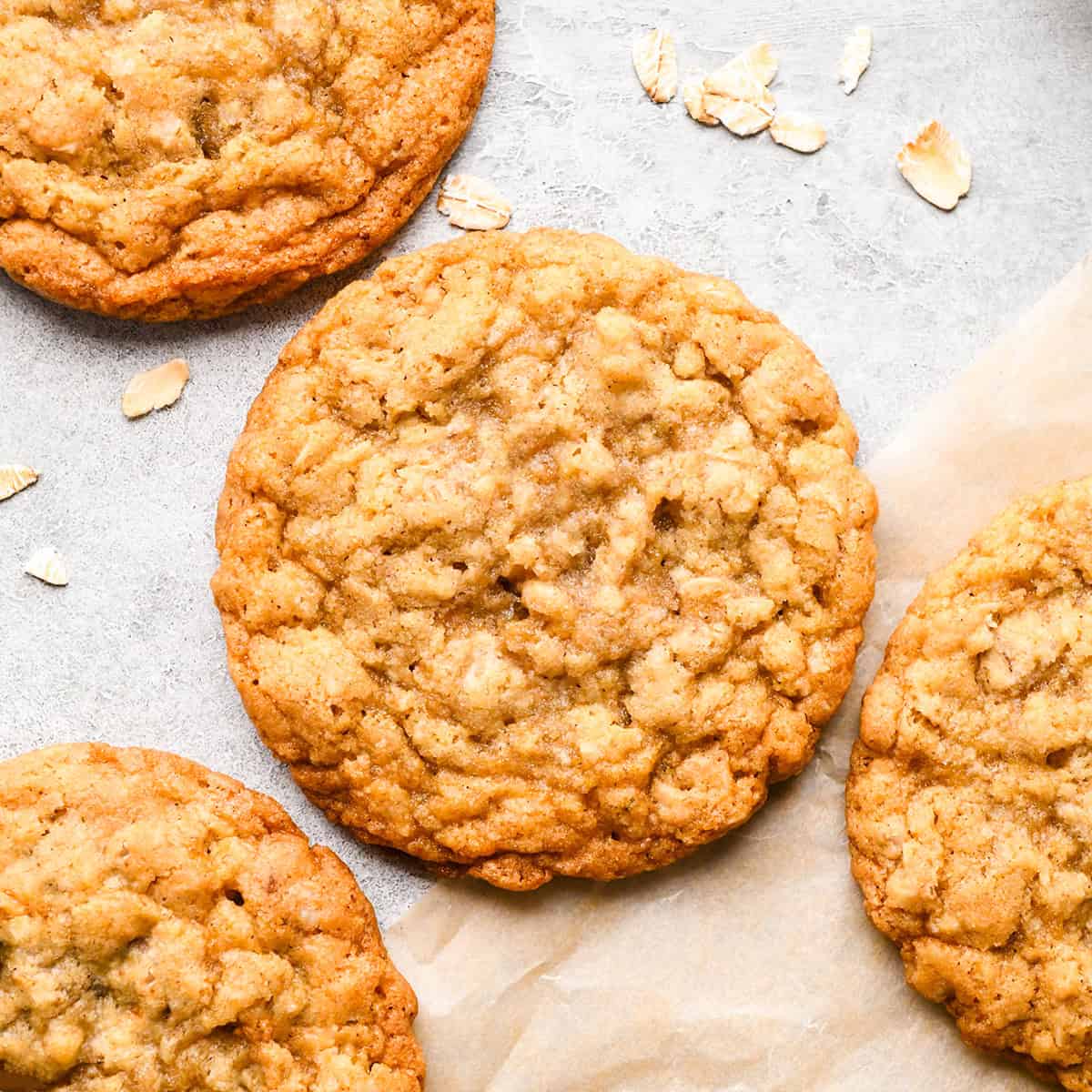 The BEST Oatmeal Cookie Recipe - crispy edges with soft and chewy centers, these oatmeal cookies are easy to make and out-of-this-world delicious. Add your favorite mix-ins for an extra special twist! #oatmealcookies #cookies #baking four oatmeal cookies on parchment paper next to a bowl of raw oats