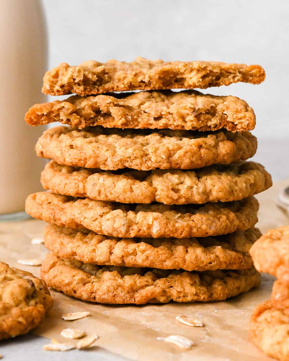 The BEST Oatmeal Cookie Recipe - crispy edges with soft and chewy centers, these oatmeal cookies are easy to make and out-of-this-world delicious. Add your favorite mix-ins for an extra special twist! #oatmealcookies #cookies #baking a stack of seven oatmeal cookies with the top cookie broken in half, placed on parchment paper with scattered oats on the paper