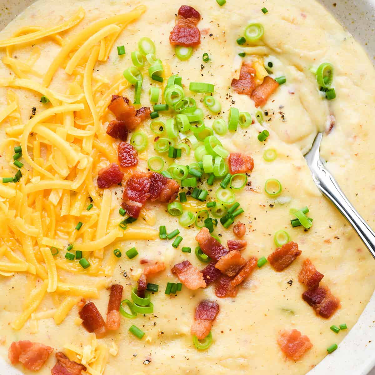 a bowl of potato soup topped with bacon, cheese, green onions and chives.