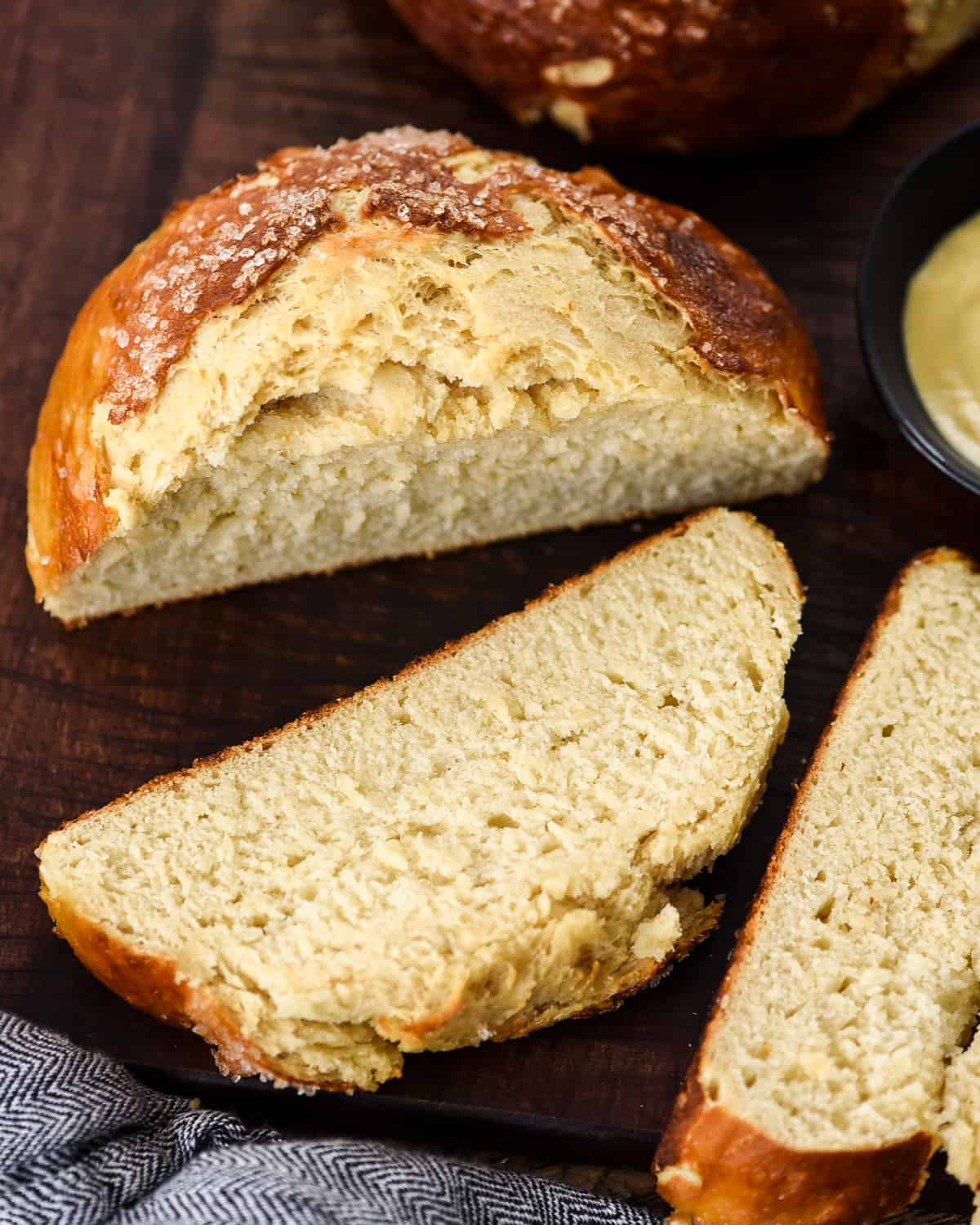 The BEST Homemade Pretzel Bread (or Pretzel Rolls) recipe ever. Seriously, once you make this you will never be able to eat store-bought pretzel bread again! It's dense, soft, chewy, buttery, salty and irresistibly delicious. Overhead view of a loaf of homemade pretzel bread on a cutting board with three slices cut and lying down near it