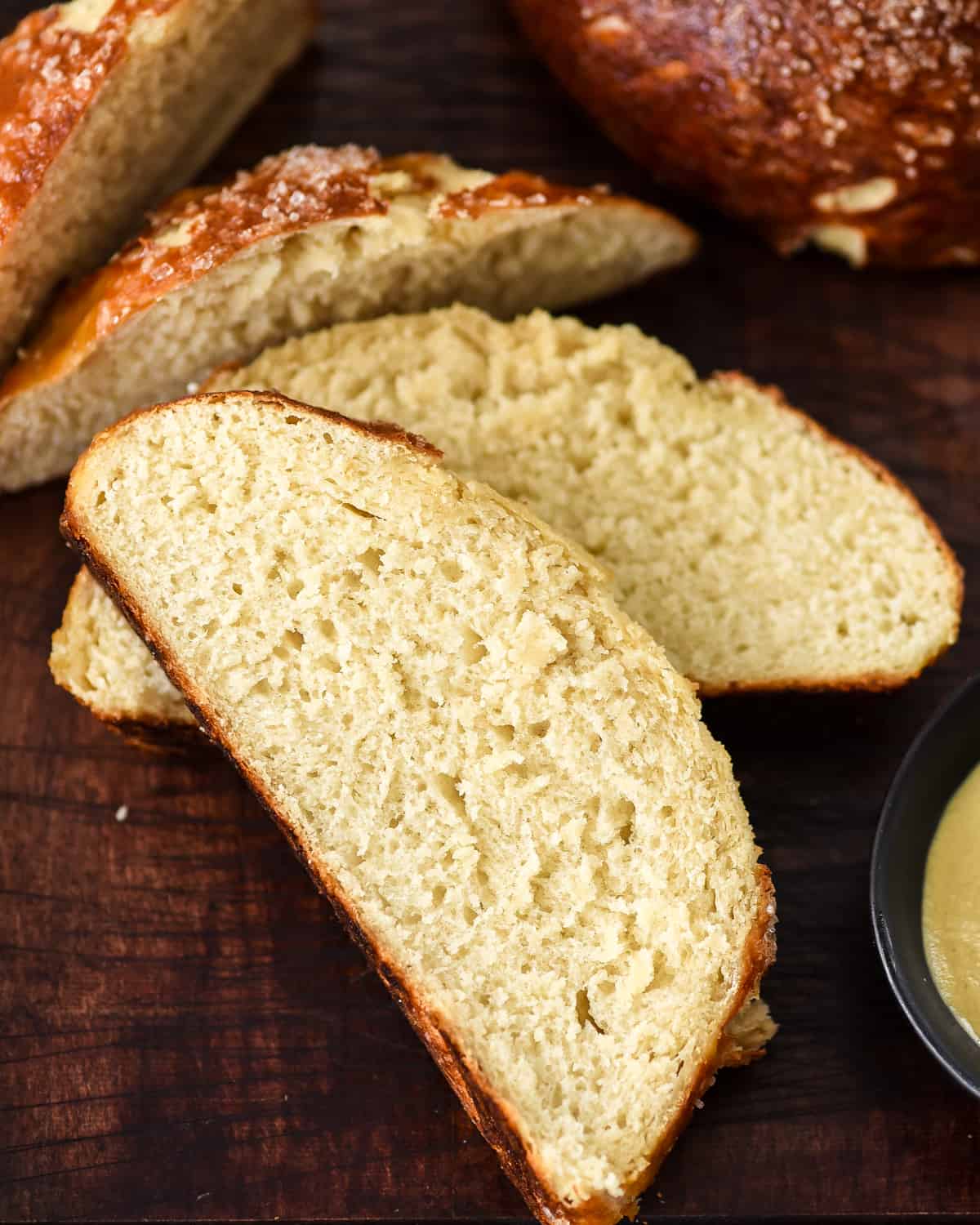The BEST Homemade Pretzel Bread recipe ever. Seriously, once you make this you will never be able to eat store-bought pretzel bread again! It's dense, soft, chewy, buttery, salty and oh-so-delicious. We've included a video with step-by-step instructions! #pretzelbread #homemade #recipe #bread #recipevideo Overhead view of three slices of homemade pretzel bread on a cutting board