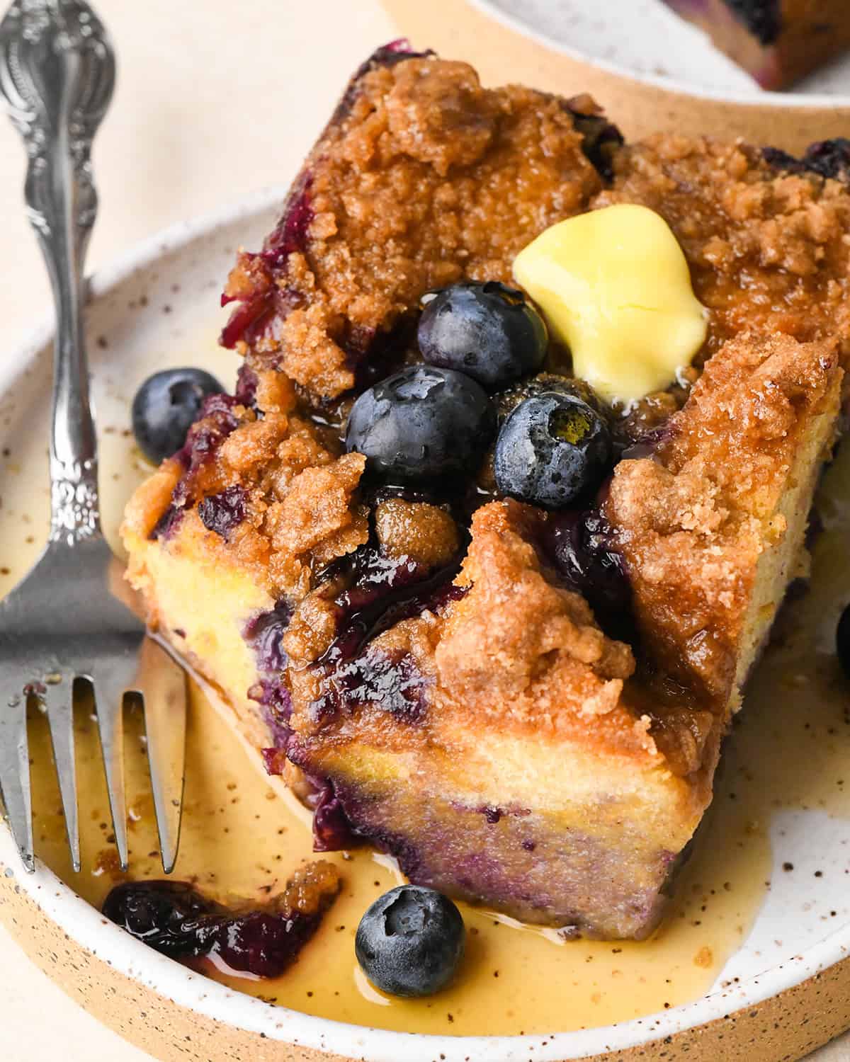a piece of Blueberry French Toast Casserole on a plate with butter, blueberries and syrup.