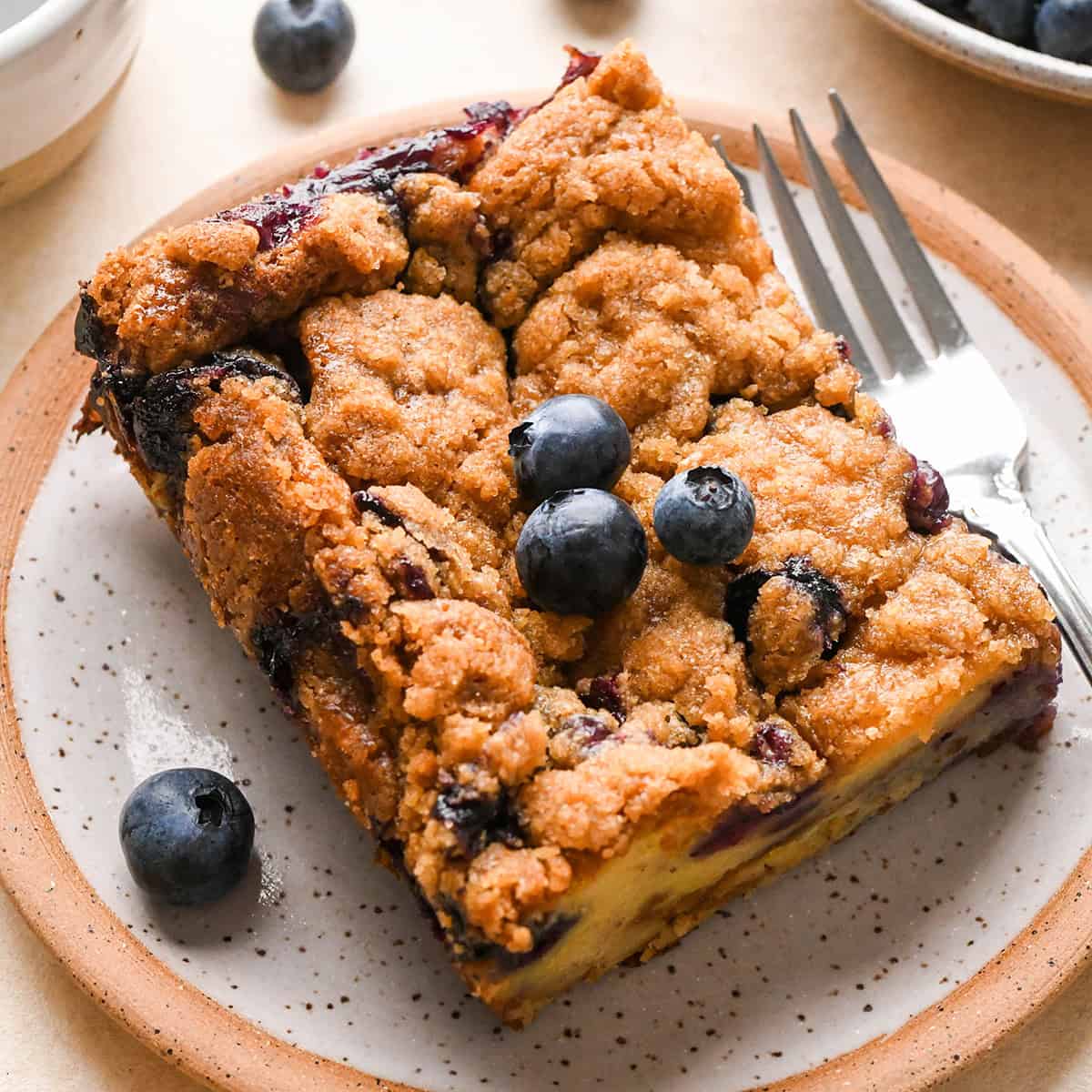 a piece of Blueberry French Toast Casserole on a plate with a fork and extra blueberries