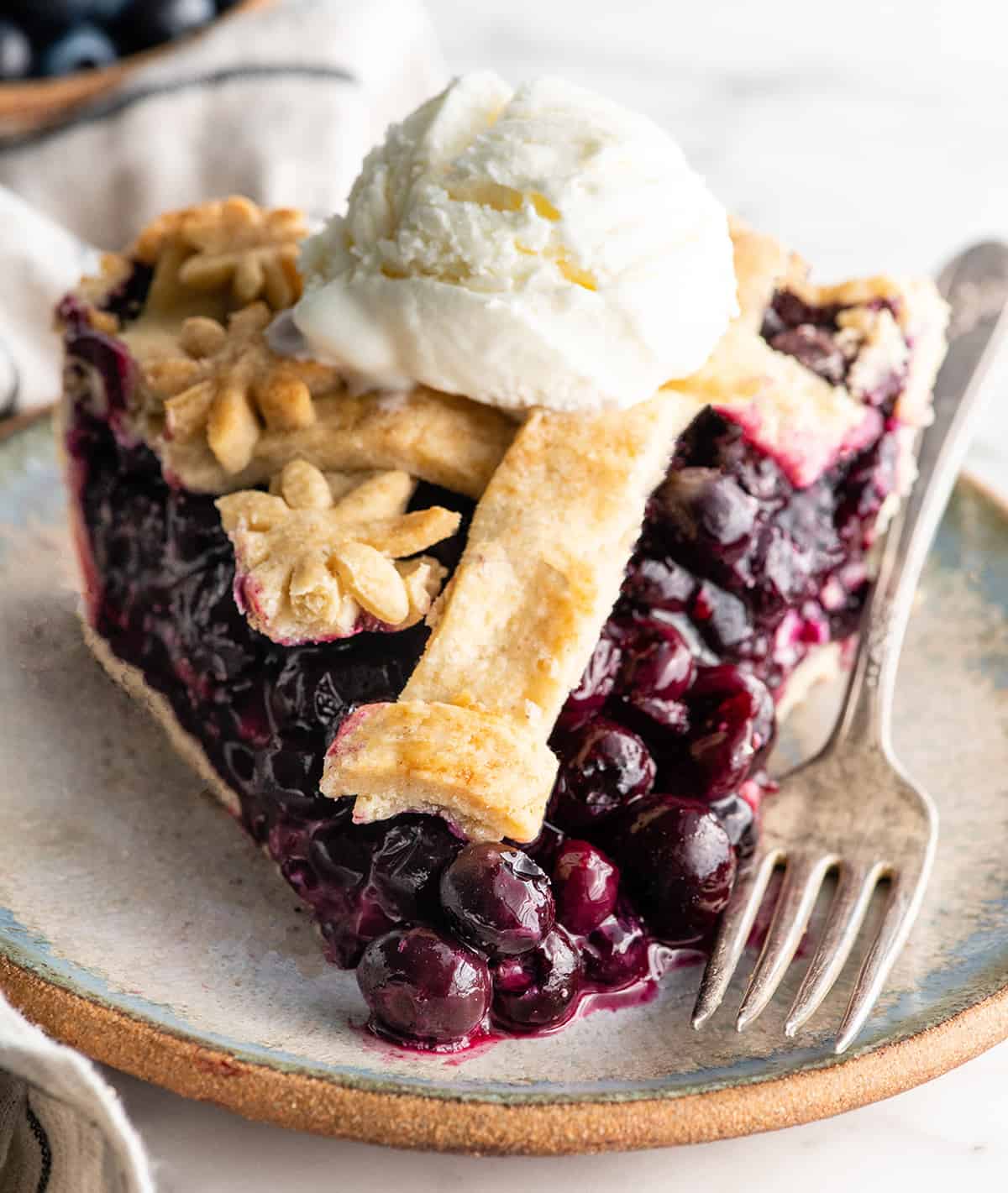 This is the best homemade Blueberry Pie Recipe you'll ever make! It's made from scratch with a fresh blueberry pie filling and NO cornstarch, and includes step-by-step instructions and photos! front view of a slice of blueberry pie with a scoop of ice cream on top