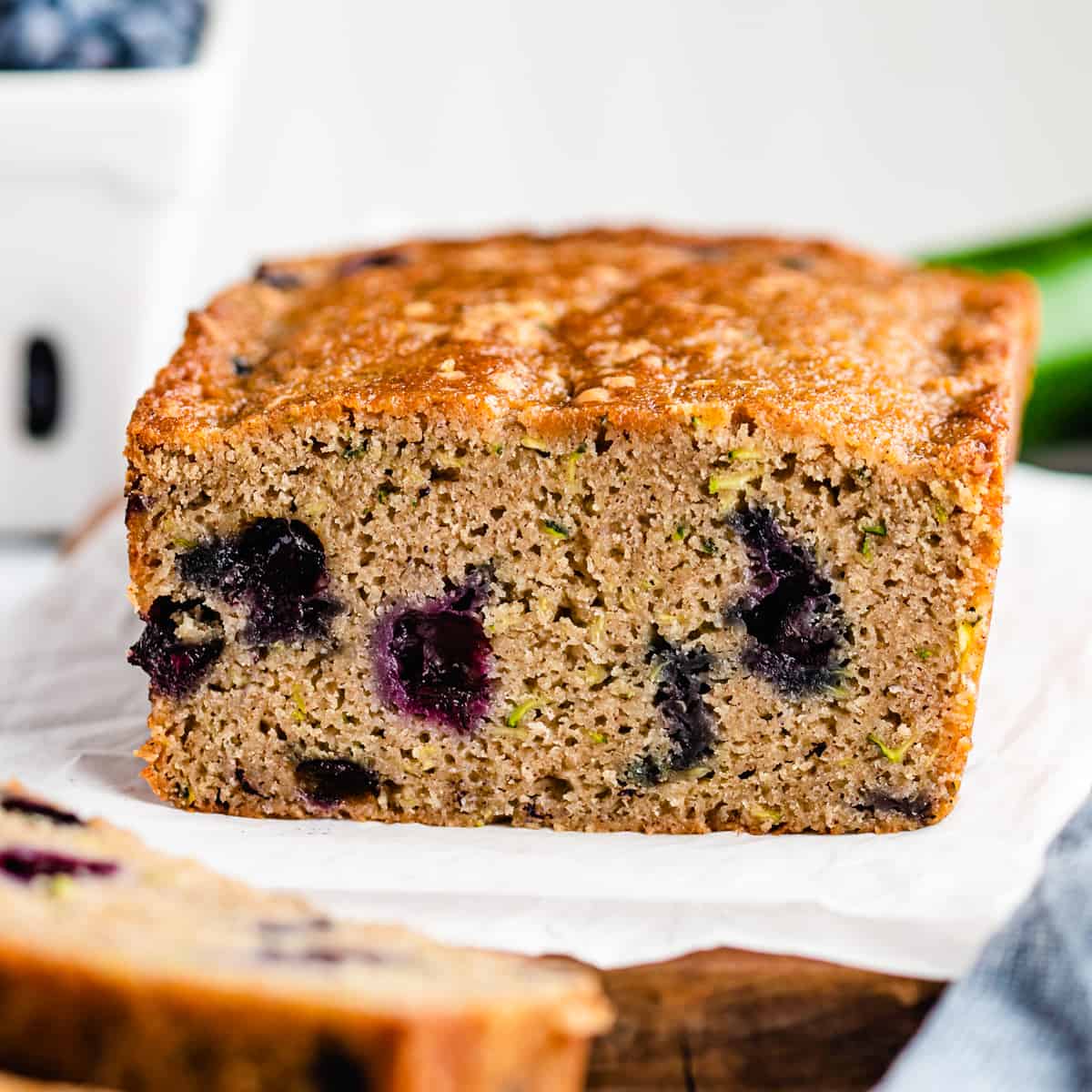 This Healthy Blueberry Zucchini Bread Recipe is the perfect breakfast or snack! It's packed full of fruits and vegetables! and is gluten-free and refined-sugar free! #glutenfree #bread #zucchini #blueberries #oatmeal #zucchinibread a loaf of Blueberry Zucchini Bread with two slices cut out of it