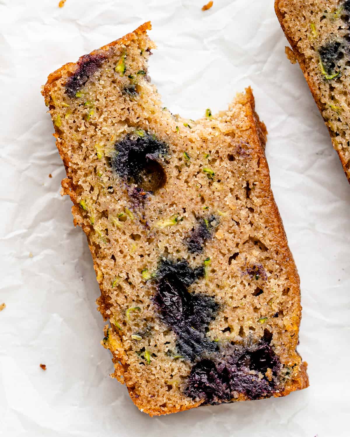 This Healthy Blueberry Zucchini Bread Recipe is the perfect breakfast or snack! It's packed full of fruits and vegetables! and is gluten-free and refined-sugar free! #glutenfree #bread #zucchini #blueberries #oatmeal #zucchinibread a slice of Blueberry Zucchini Bread with a bite taken out of it