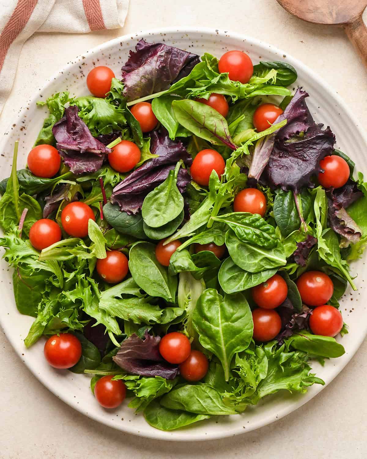 This Burrata Salad Recipe is made with homemade croutons, homemade balsamic vinaigrette dressing tomatoes and spring mix. It's a simple yet elegant salad that serves a crowd! #burrata #burratacheese #burratasalad #capresesald #saladrecipe #summer #summersalad how to assemble burrata salad - tomatoes and spring mix on a plate