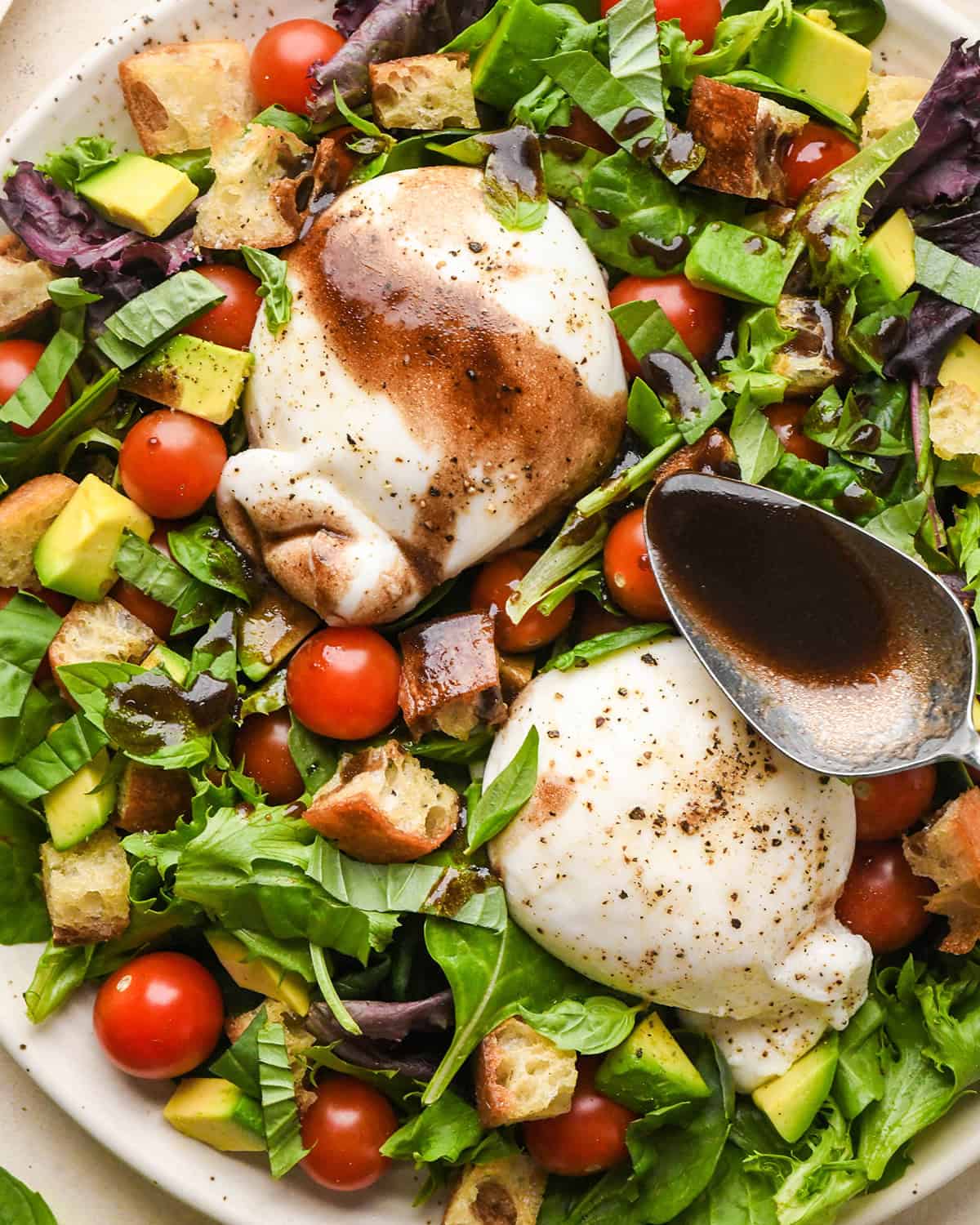 dressing being poured over burrata salad assembled on a large serving plate