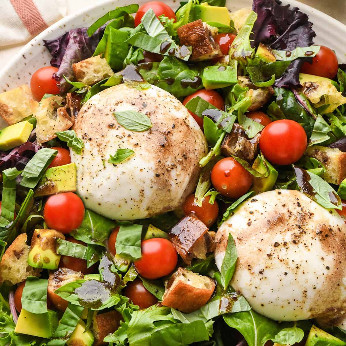 This Burrata Salad Recipe is made with homemade croutons, homemade balsamic vinaigrette dressing tomatoes and spring mix. It's a simple yet elegant salad that serves a crowd! #burrata #burratacheese #burratasalad #capresesald #saladrecipe #summer #summersalad burrata salad on in a serving dish with balsamic vinaigrette dressing