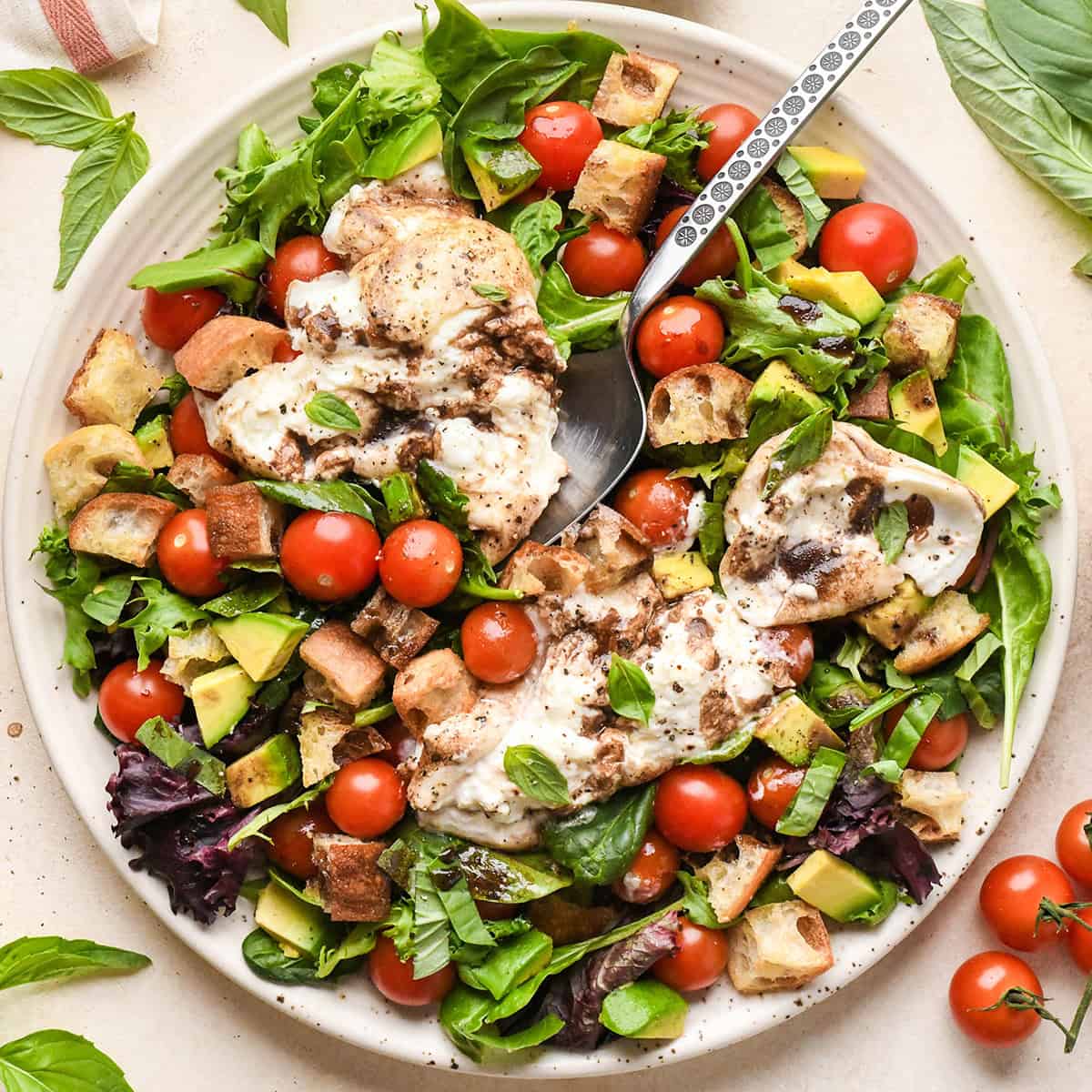 Burrata Salad on a serving plate with a serving spoon and the burrata opened