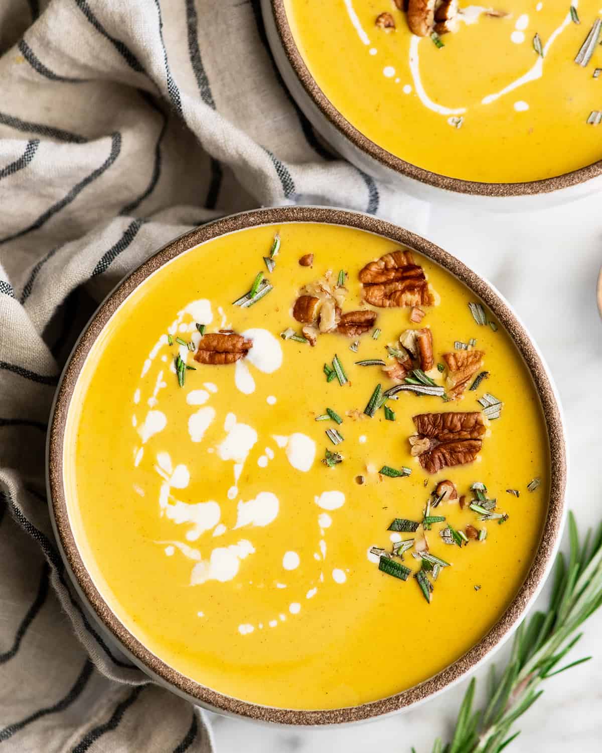 This is the Best Butternut Squash Soup Recipe ever! Celery, onion and carrots give this squash soup a beautiful depth of flavor. It's silky-smooth and perfectly sweet with a touch of fall spices. This butternut soup is easy to make in one pot with either an immersion blender or standard blender. Overhead view of a bowl of butternut squash soup with cream, herbs and nuts