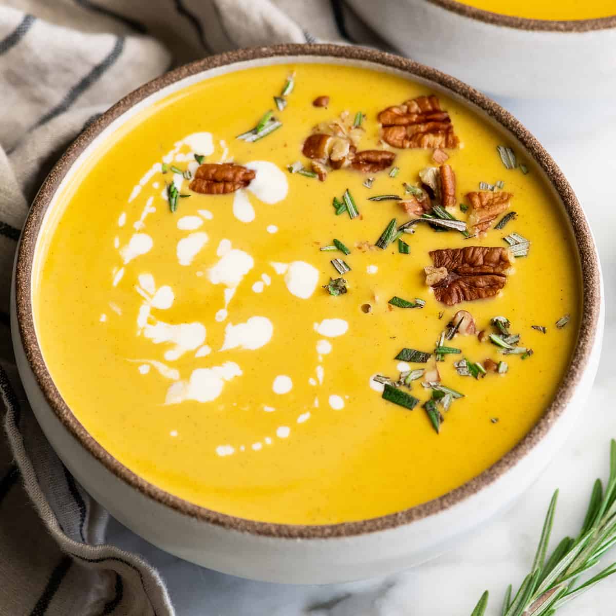 This is the Best Butternut Squash Soup Recipe ever! Celery, onion and carrots give this squash soup a beautiful depth of flavor. It's silky-smooth and perfectly sweet with a touch of fall spices. This butternut soup is easy to make in one pot with either an immersion blender or standard blender. front view of a bowl of butternut squash soup with cream, herbs and nuts