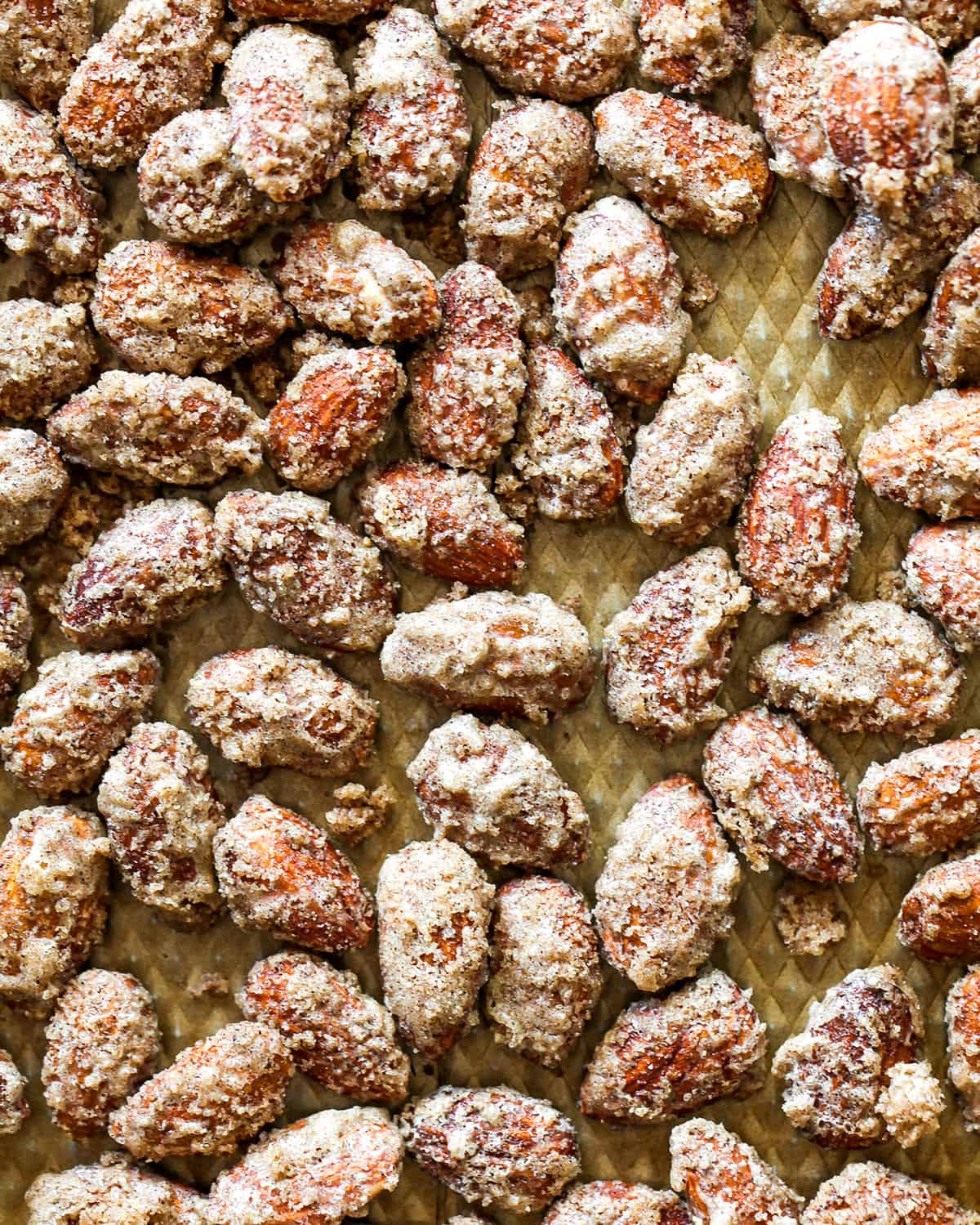 This Candied Almonds Recipe is easy to make with just 6 ingredients. These cinnamon roasted almonds are even more delicious than the nuts you can get at the mall or fair, and they're freezer-friendly so you can make a batch and enjoy them for months as a snack, on top of salads, etc. overhead view of candied almonds after roasting on a baking sheet