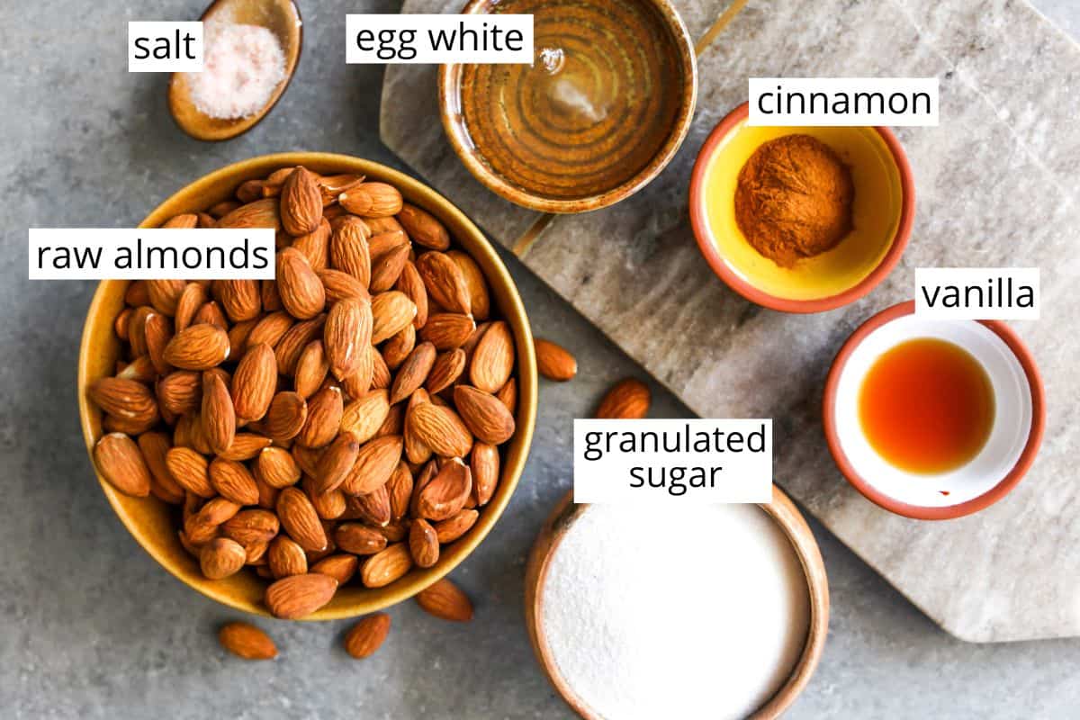 This Candied Almonds Recipe is easy to make with just 6 ingredients. These cinnamon roasted almonds are even more delicious than the nuts you can get at the mall or fair, and they're freezer-friendly so you can make a batch and enjoy them for months as a snack, on top of salads, etc. overhead view of the labeled ingredients in this candied almonds recipe