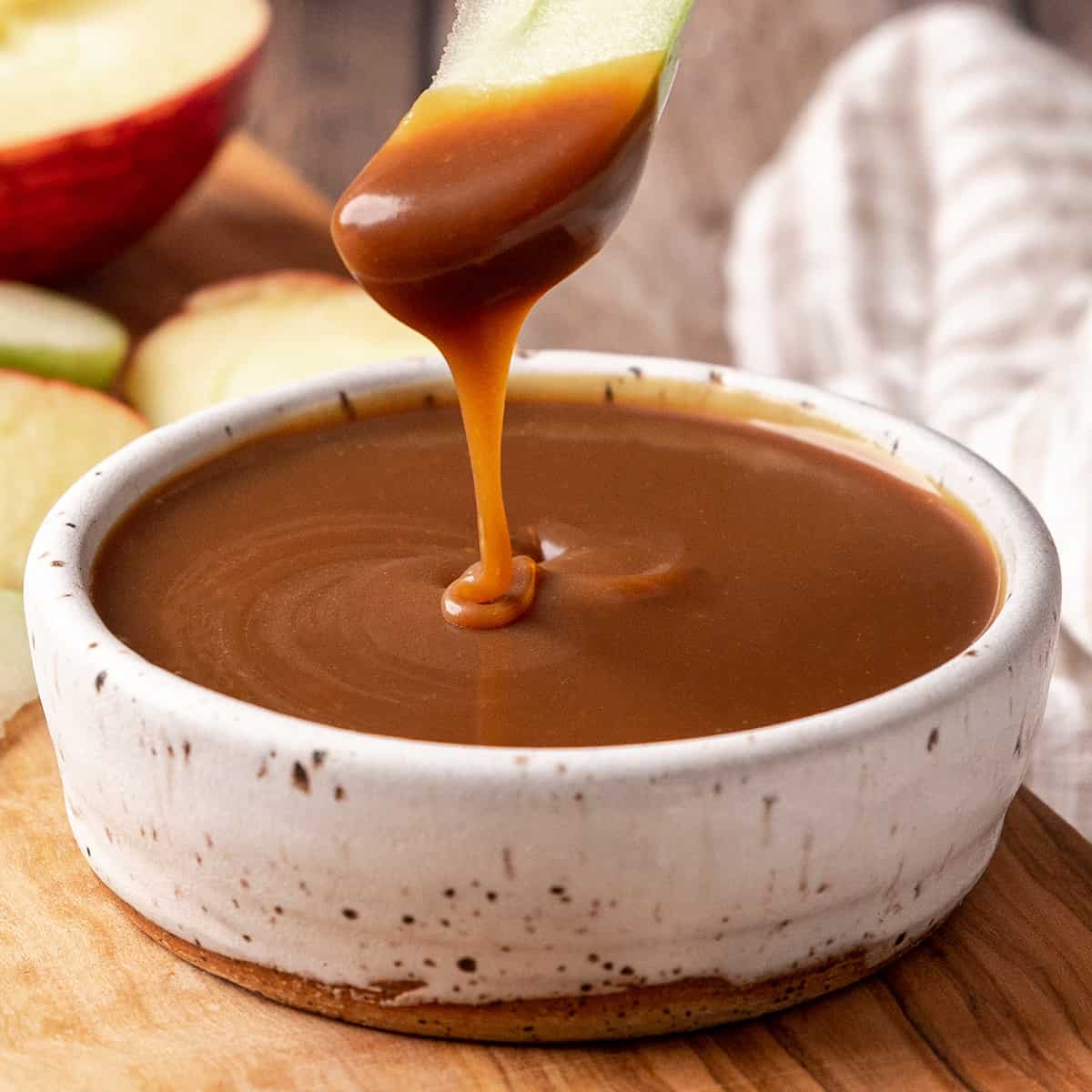 an apple right after it was dipped into a bowl of Caramel Apple Dip below