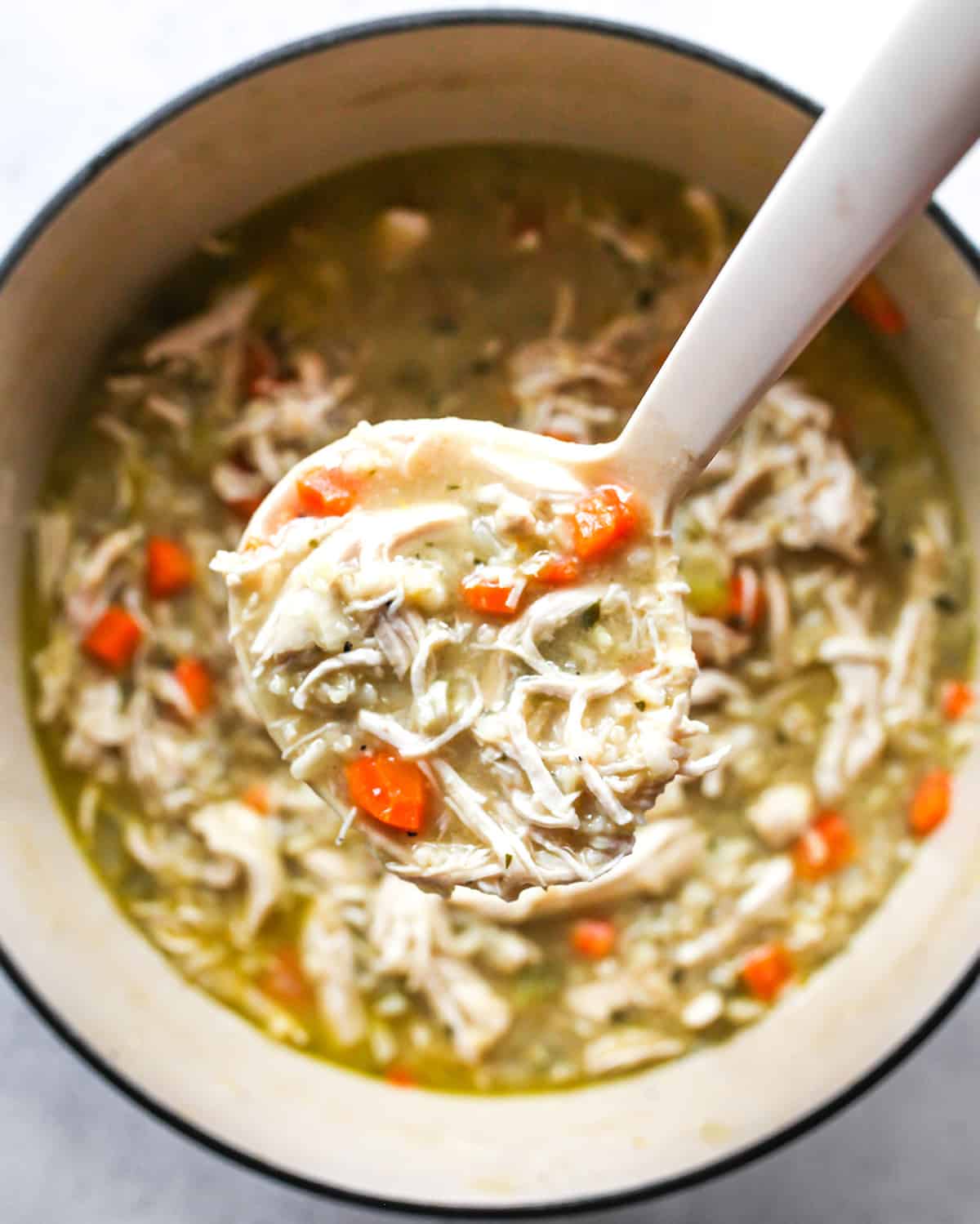 This Chicken and Rice Soup is flavorful, hearty, healthy and it's made in one pot in under an hour! Chicken and wild rice soup is a perfect meal for busy, chilly nights, it makes great leftovers & freezes well too! Overhead view of a ladle scooping chicken and rice soup out of a pot