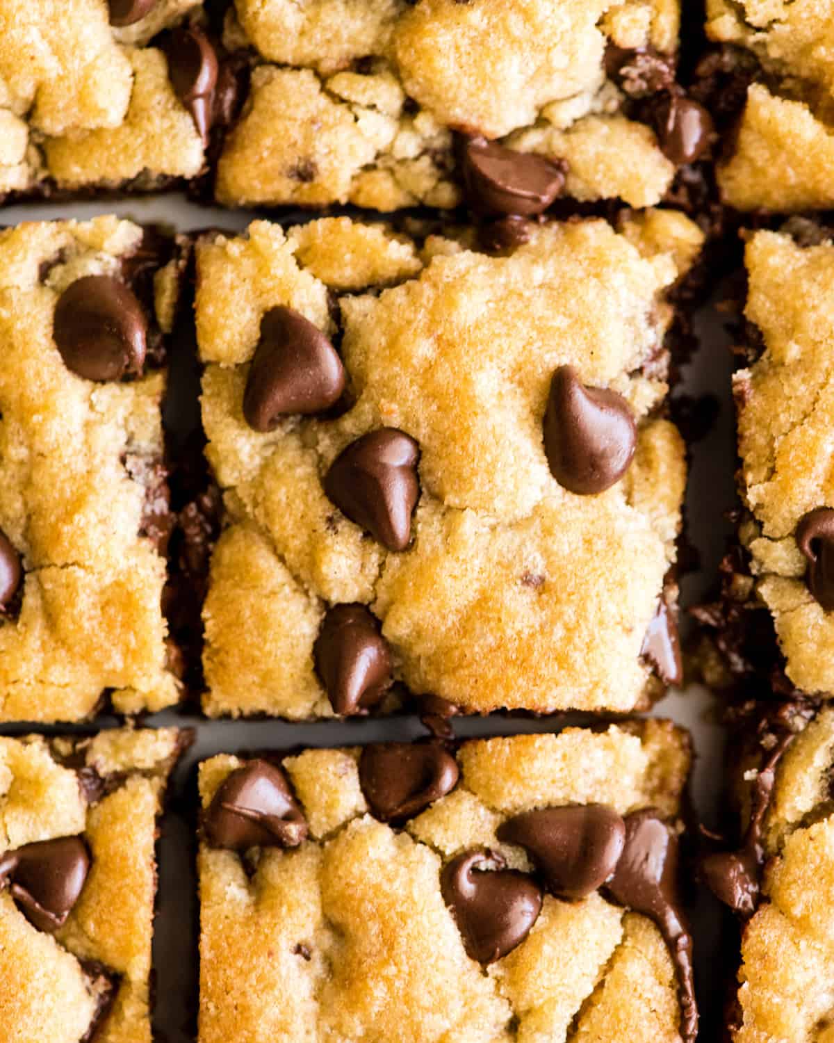 These are the absolute best chocolate chip cookie bars EVER. This cookie bar recipe is easy to make (5 minutes to mix, 20 minutes to bake) and results in a gooey, chewy, doughy yet fully cooked chocolate chip cookie bar that is 100% irresistible. Serve warm with a scoop of ice cream! #chocolatechipcookiebars #cookiebars #cookeis #dessert #baking overhead view of 9 chocolate chip cookie bars