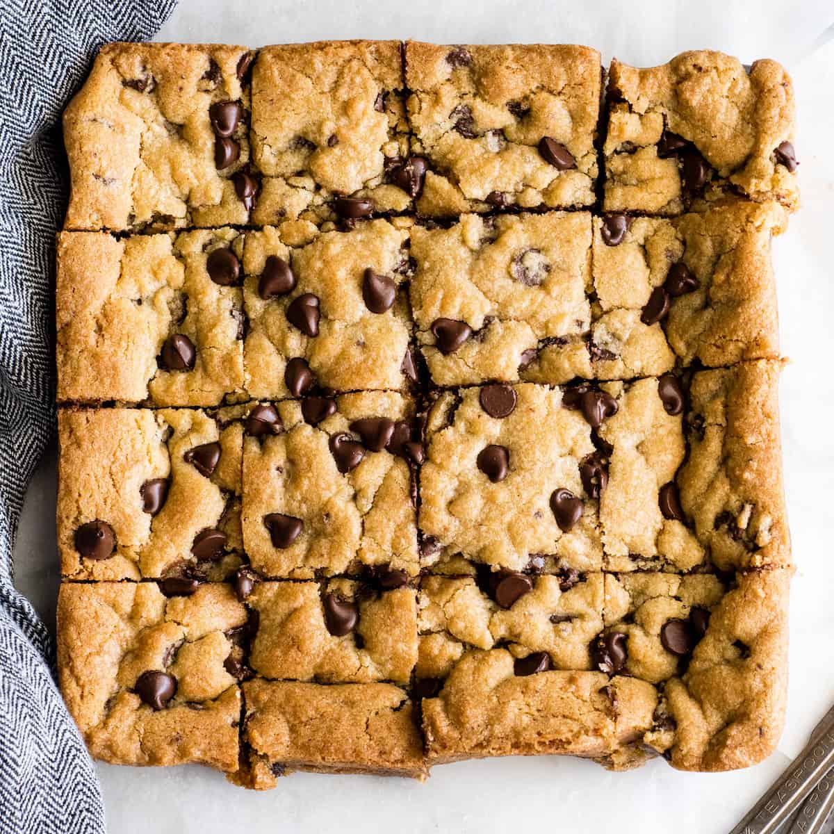 These are the absolute best chocolate chip cookie bars EVER. This cookie bar recipe is easy to make (5 minutes to mix, 20 minutes to bake) and results in a gooey, chewy, doughy yet fully cooked chocolate chip cookie bar that is 100% irresistible. Serve warm with a scoop of ice cream! #chocolatechipcookiebars #cookiebars #cookeis #dessert #baking overhead view of 16 chocolate chip cookie bars cut into squares